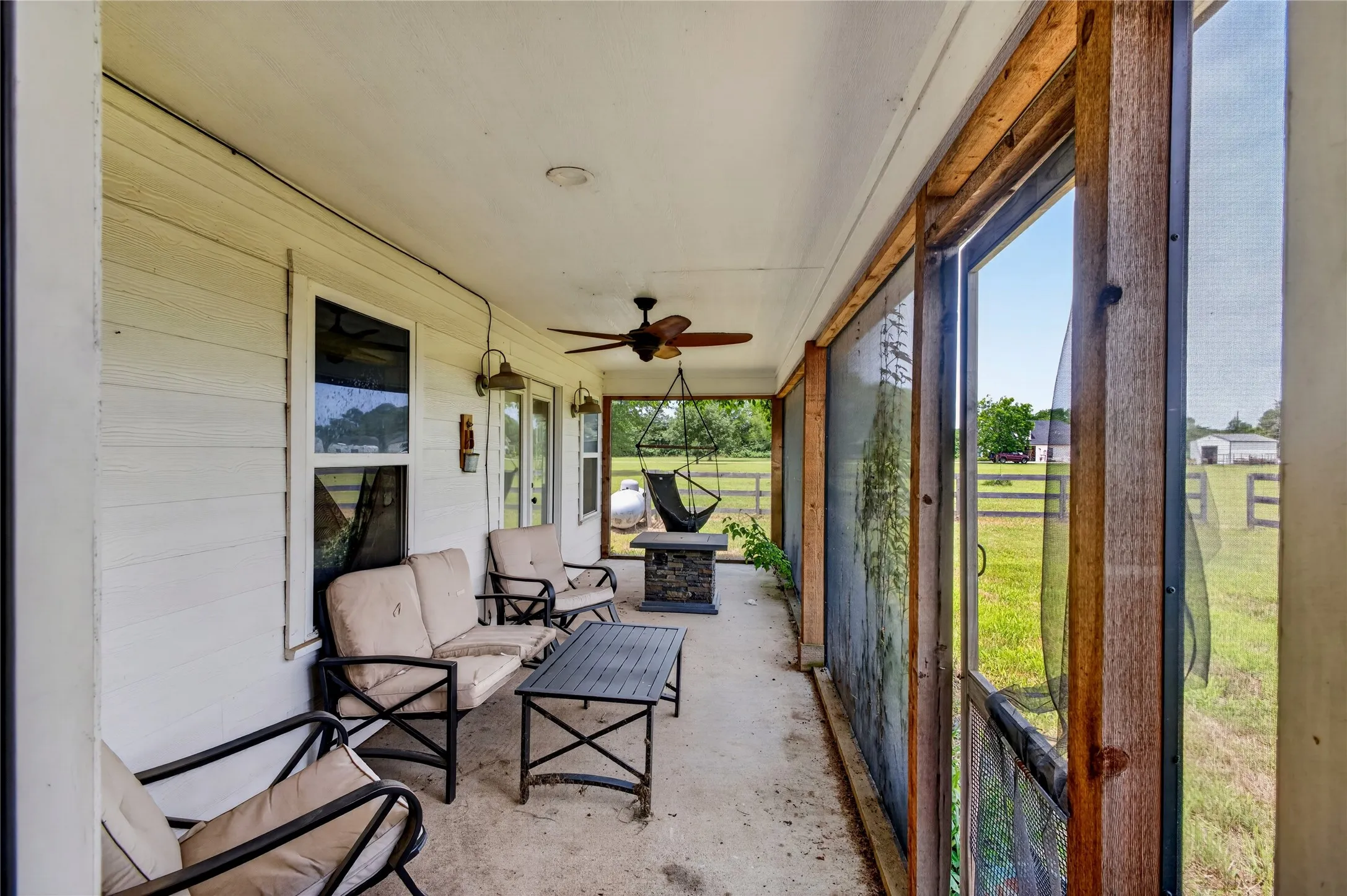 Spacious screened porch featuring a concrete slab, wooden beams, a ceiling fan, and exterior wall lighting