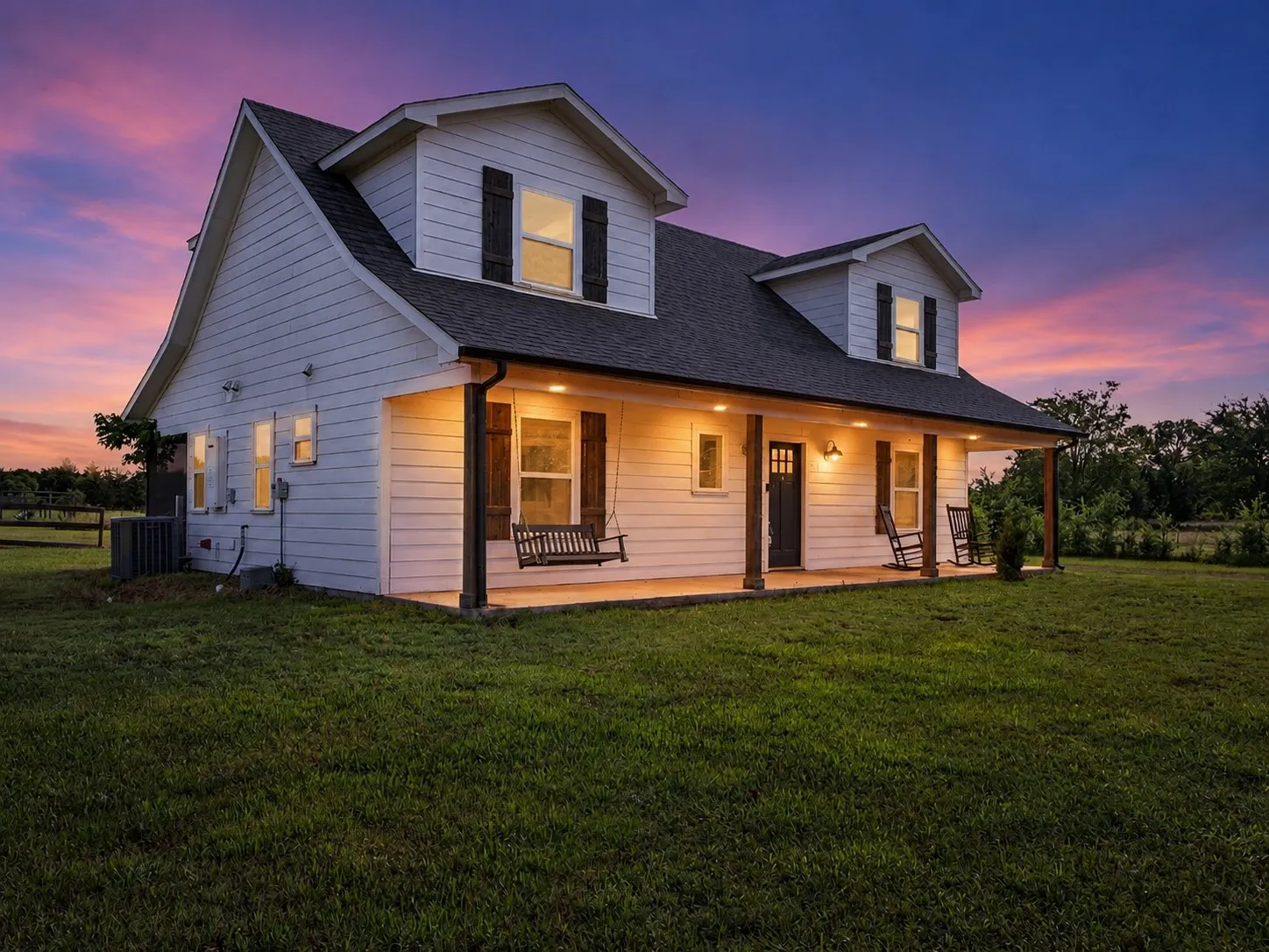 White clapboard exterior with dark shutters, a covered porch with recessed lighting, and wooden support pillars