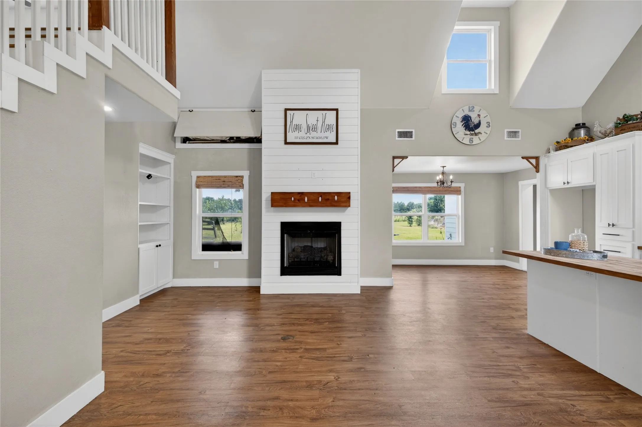 Spacious open-concept living area featuring wood-finish flooring and a central fireplace with shiplap surround and wood mantel