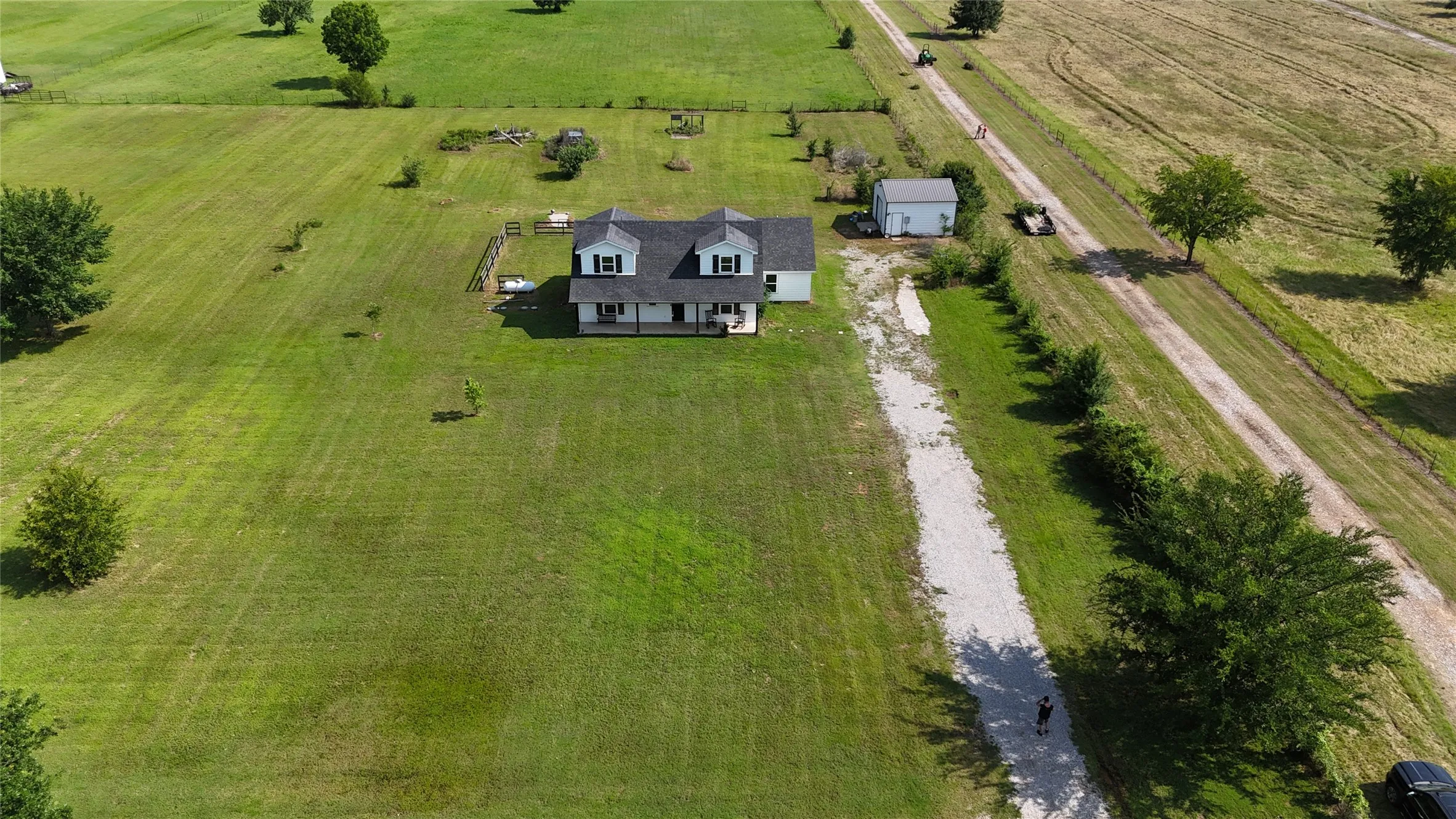 Expansive green property featuring a two-story residence with a covered front porch, dormer windows, and a detached outbuilding