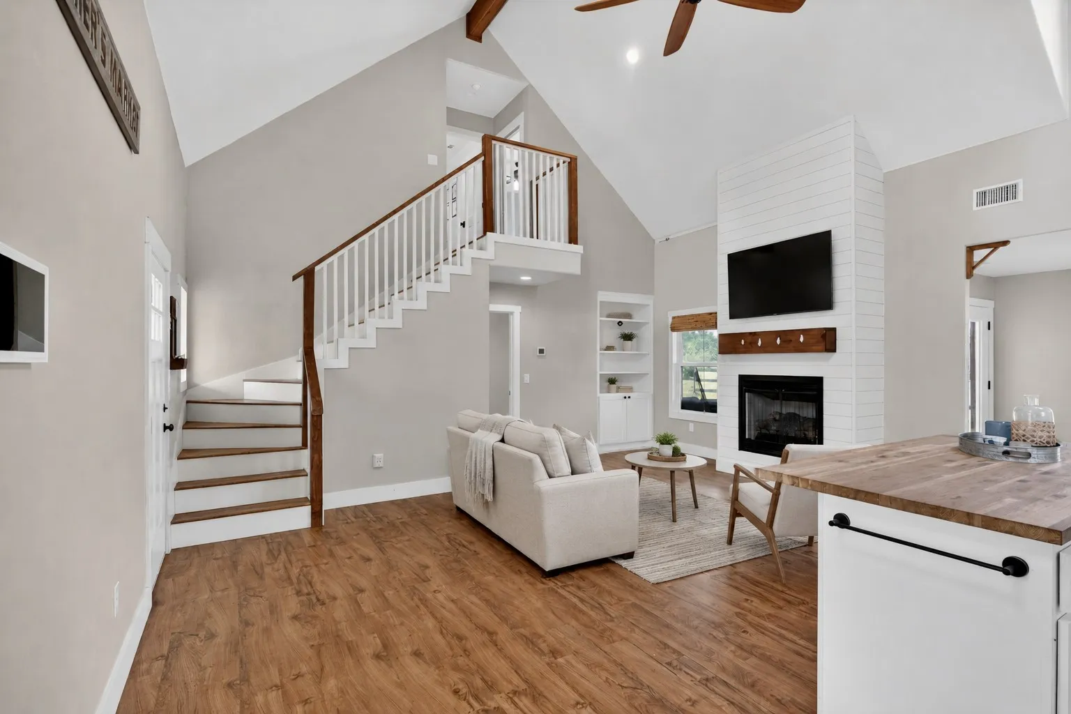 Spacious living area featuring vaulted ceilings, wood-finish flooring, and a white shiplap fireplace with a wood mantle