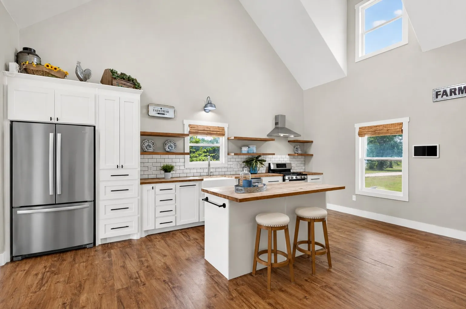 Kitchen featuring vaulted ceilings, wood-finish flooring, white cabinetry, stainless steel appliances, and a central island with a wood countertop. Some elements are virtually staged.