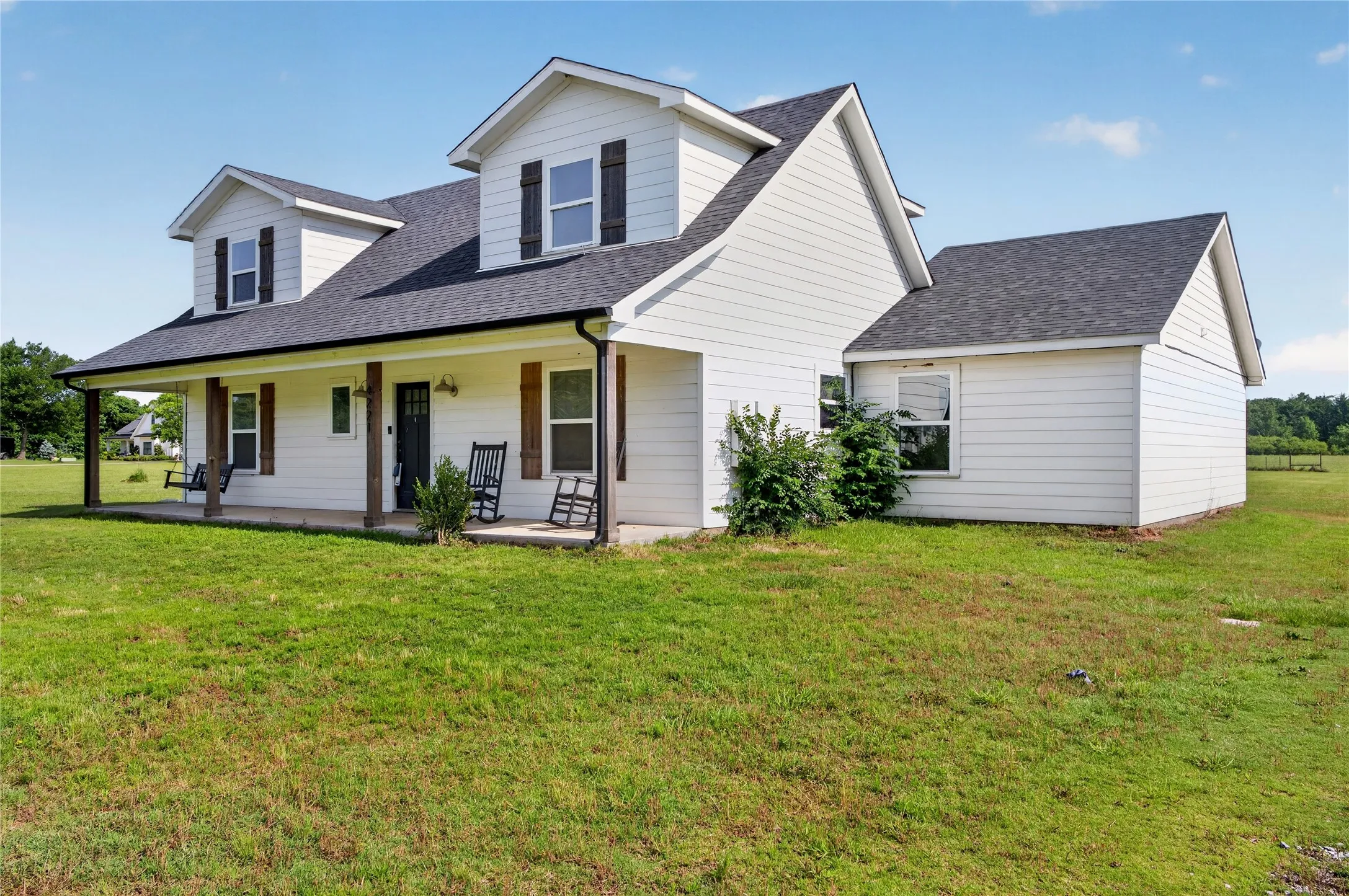 White siding exterior with a dark shingle roof and a covered front porch supported by wood-look columns