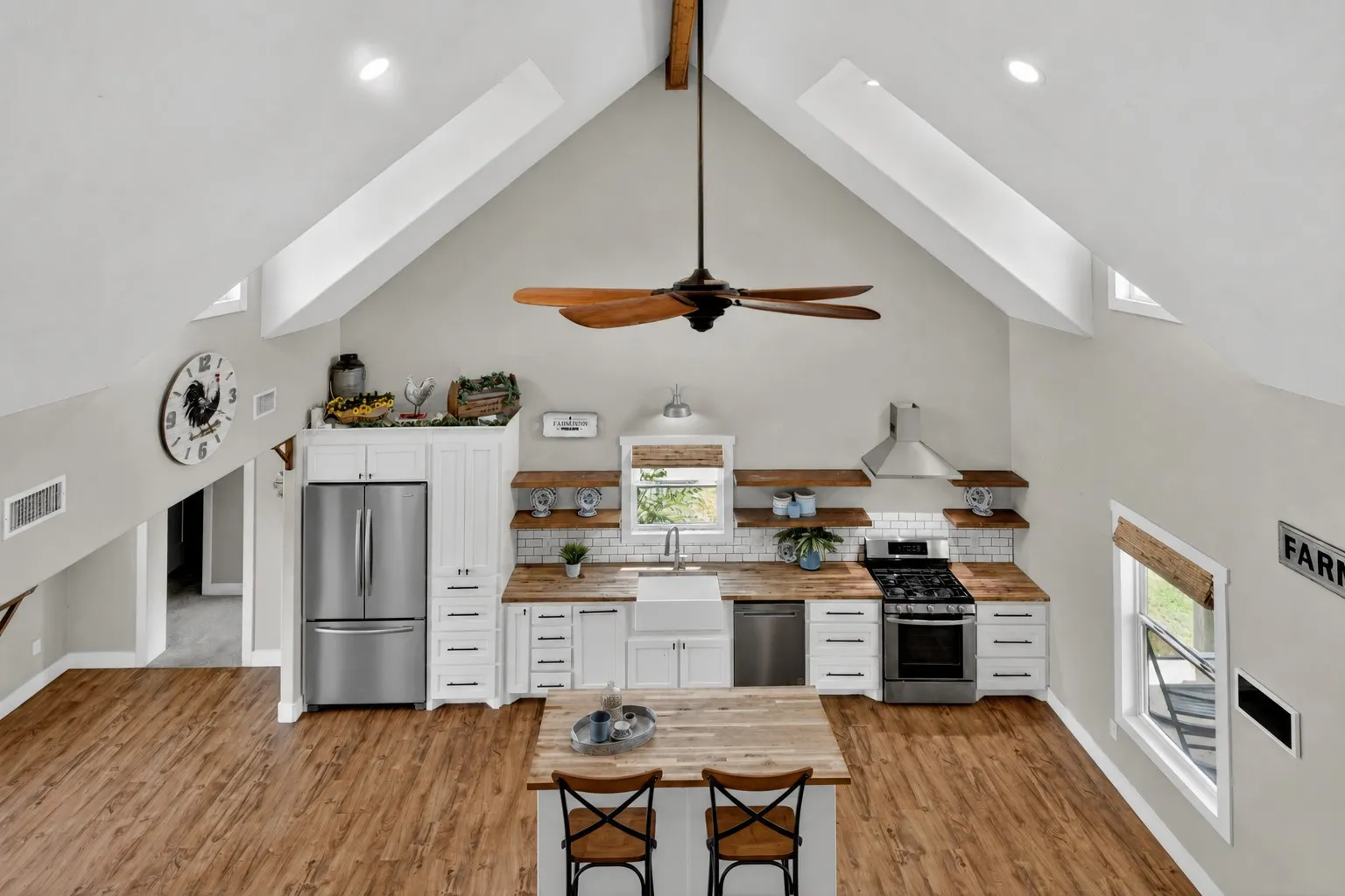 Vaulted ceilings defining a spacious kitchen featuring wood-finish flooring, white cabinetry, stainless steel appliances, and wood countertops
