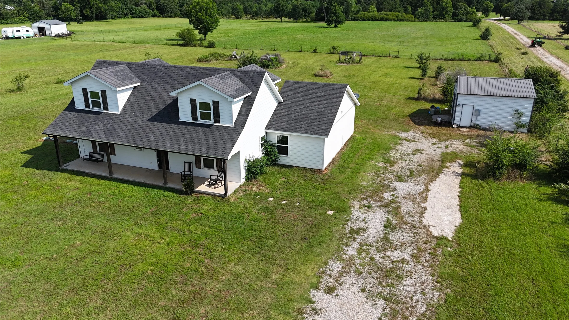 White siding residence featuring a dark shingle roof, two dormer windows with black shutters, and a covered front porch with dark support columns