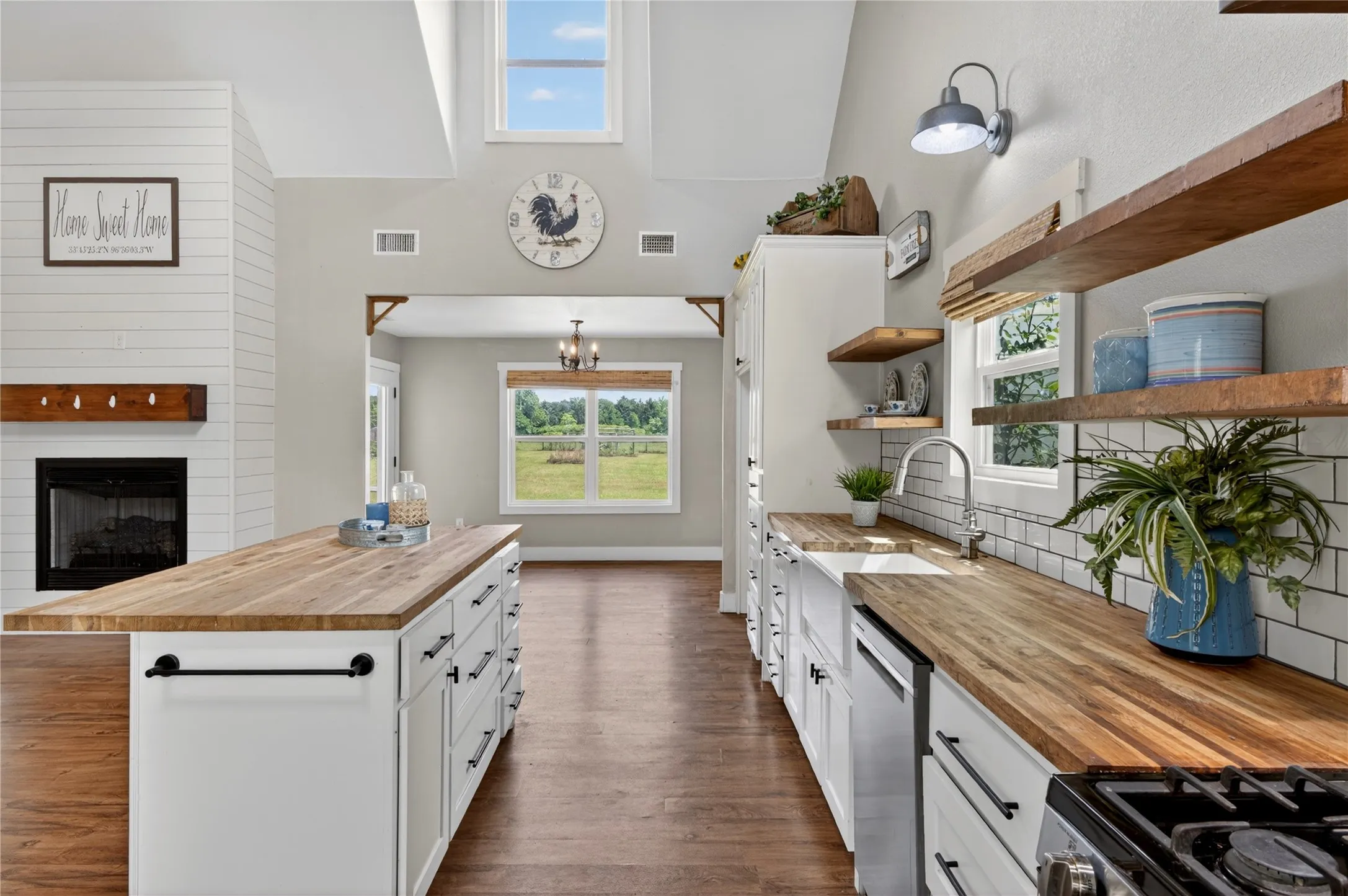 Open-concept kitchen featuring wood-finish flooring, butcher block countertops, white shaker cabinetry, an integrated sink, and an expansive kitchen island with storage