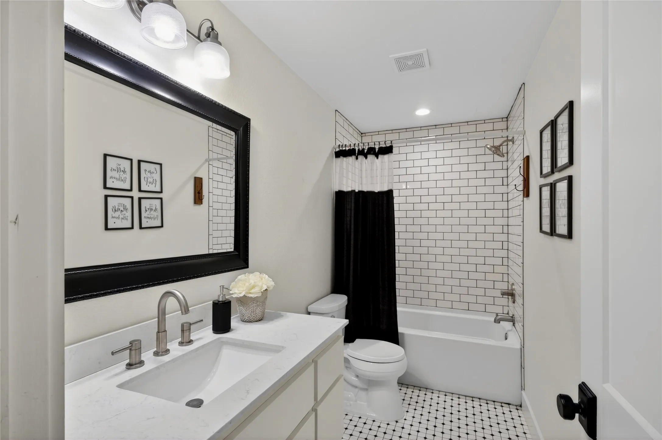 Bathroom featuring a white subway tile shower surround, integrated white vanity sink with brushed nickel fixtures, and a black and white mosaic tile floor