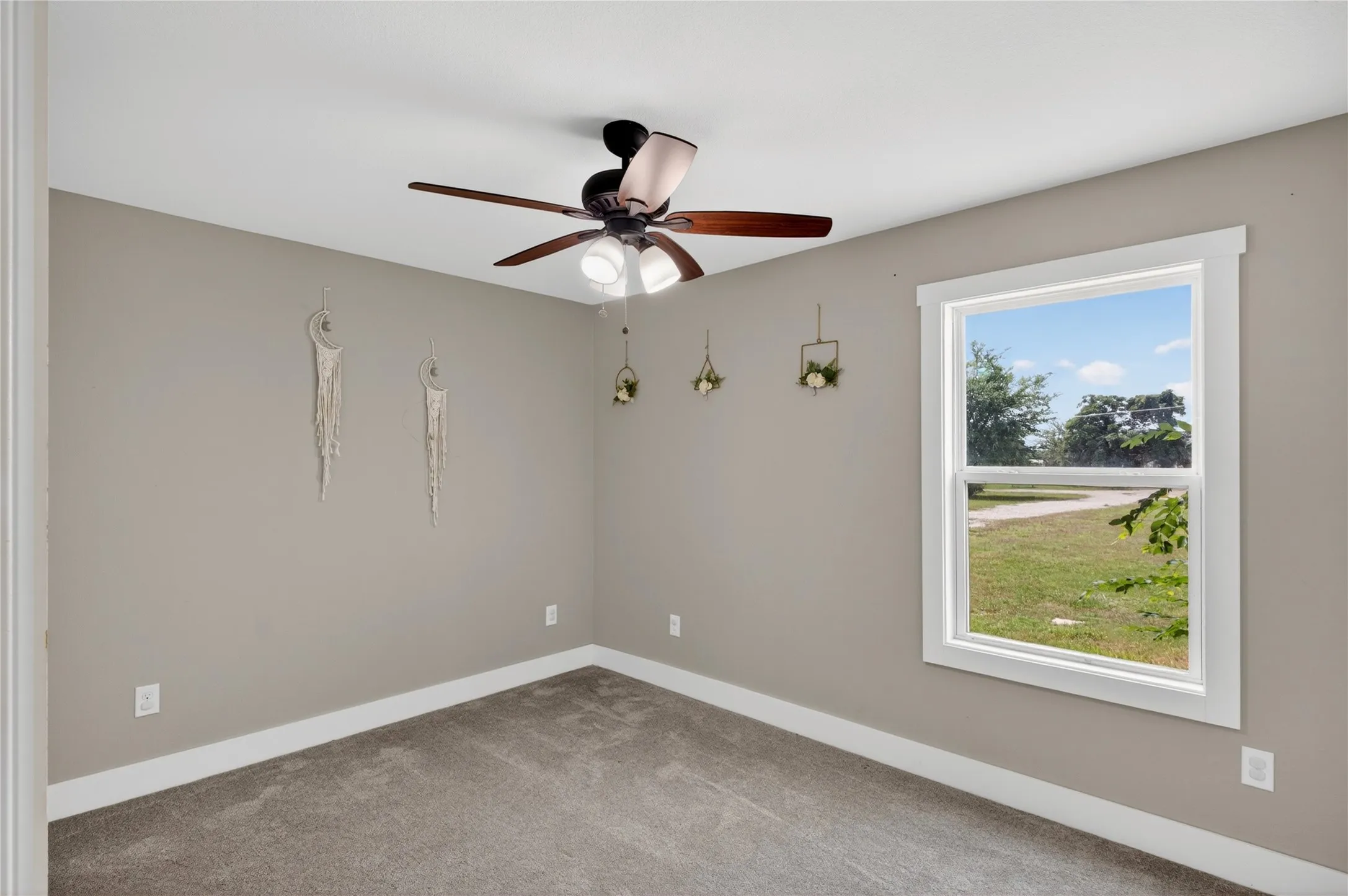 Carpeted room featuring a ceiling fan with integrated lighting, a double-hung window with white trim, and neutral wall tones