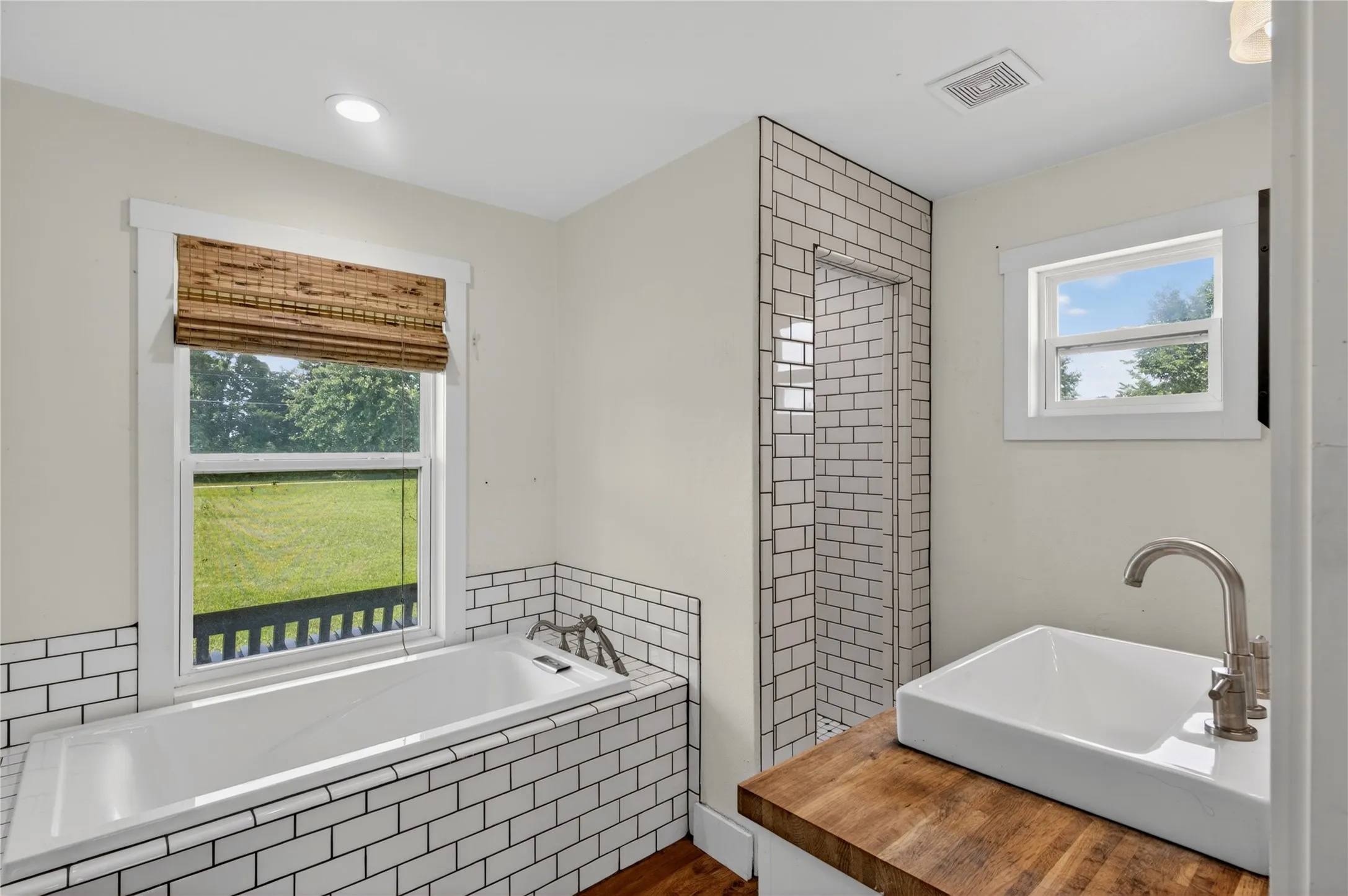 Bathroom featuring subway tile accents, a built-in tub with a window, a walk-in shower, a vessel sink, and wood-finish countertop