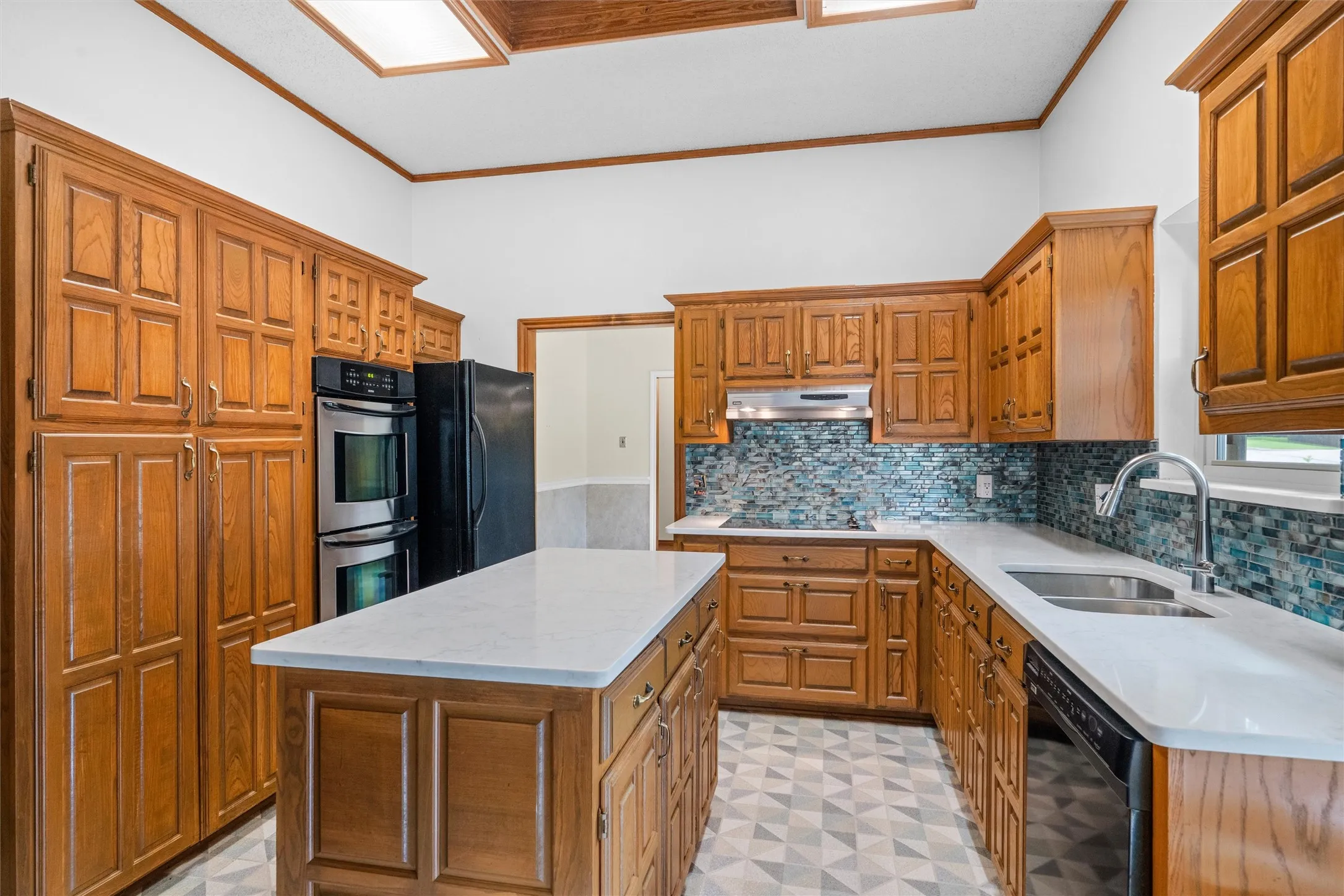 Kitchen featuring extensive wood cabinetry, white countertops, a mosaic tile backsplash, double wall ovens, and a central island