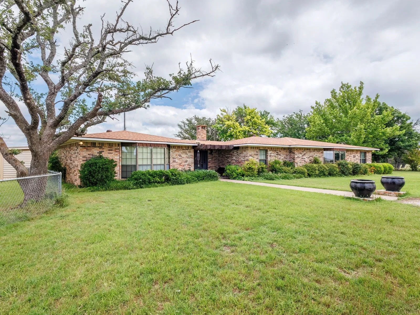 Brick exterior home featuring a composition shingle roof, established landscaping, and a concrete walkway