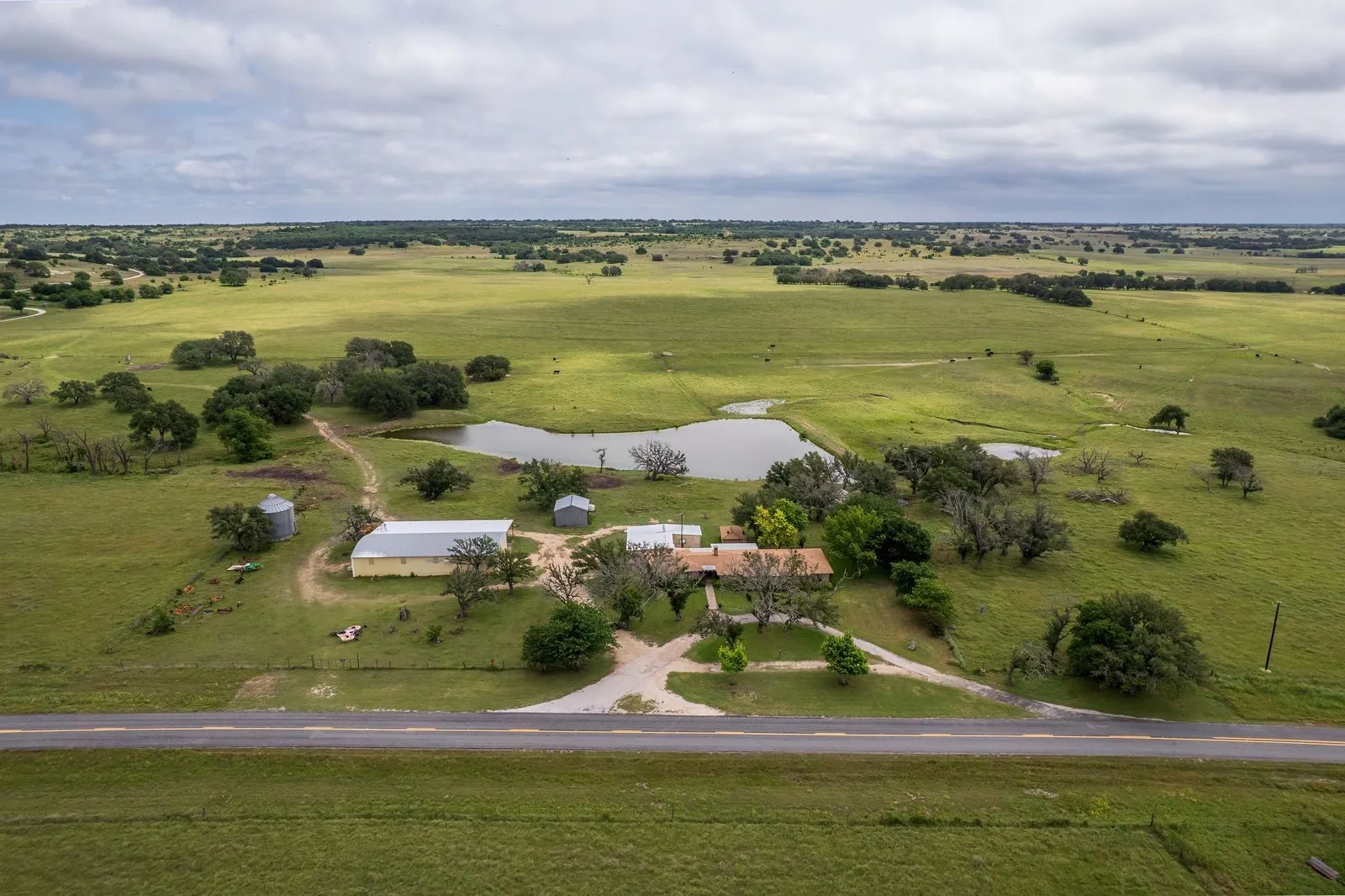Expansive acreage featuring multiple structures, including a primary residence with a brown roof, a large yellow outbuilding, and additional smaller outbuildings