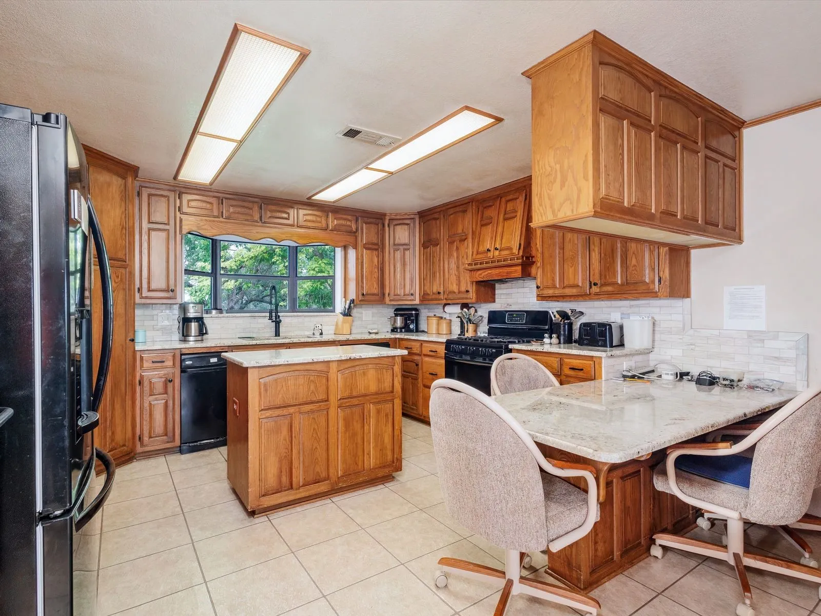 Kitchen featuring wood cabinetry, a center island with countertop, tile flooring, and black appliances