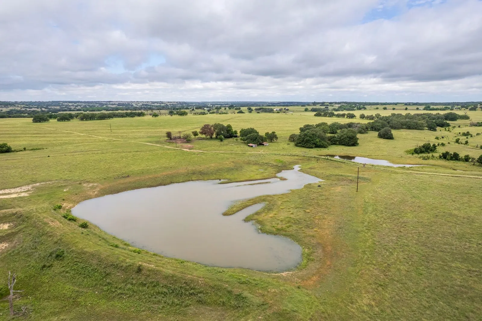 Expansive acreage featuring multiple ponds, scattered mature trees, and a distant building