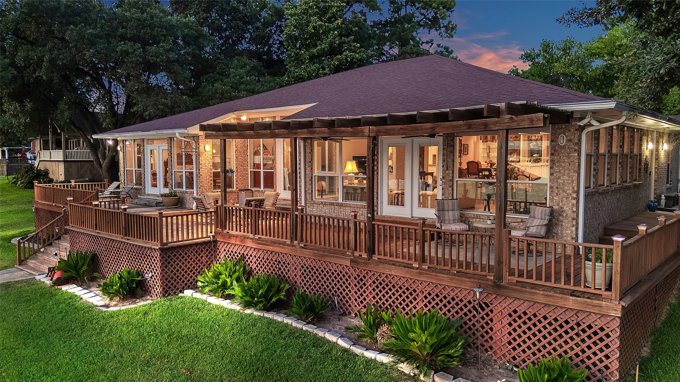 Back of house at dusk with french doors, pergola and open decks on 3 sides of home