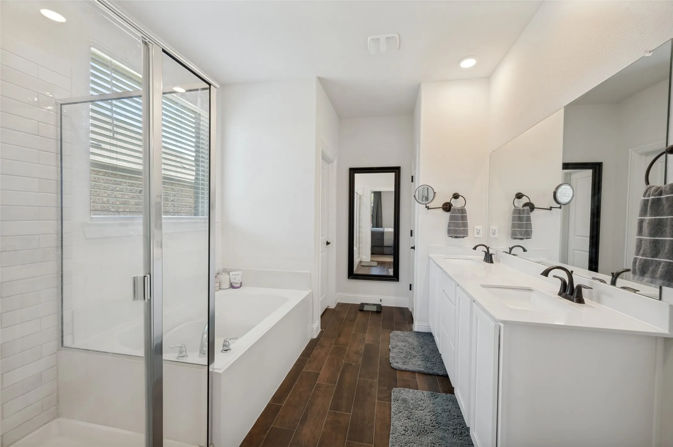 Modern bathroom featuring a dual vanity with white cabinetry and integrated sinks, matte black fixtures, an expansive mirror, and wood-finish flooring