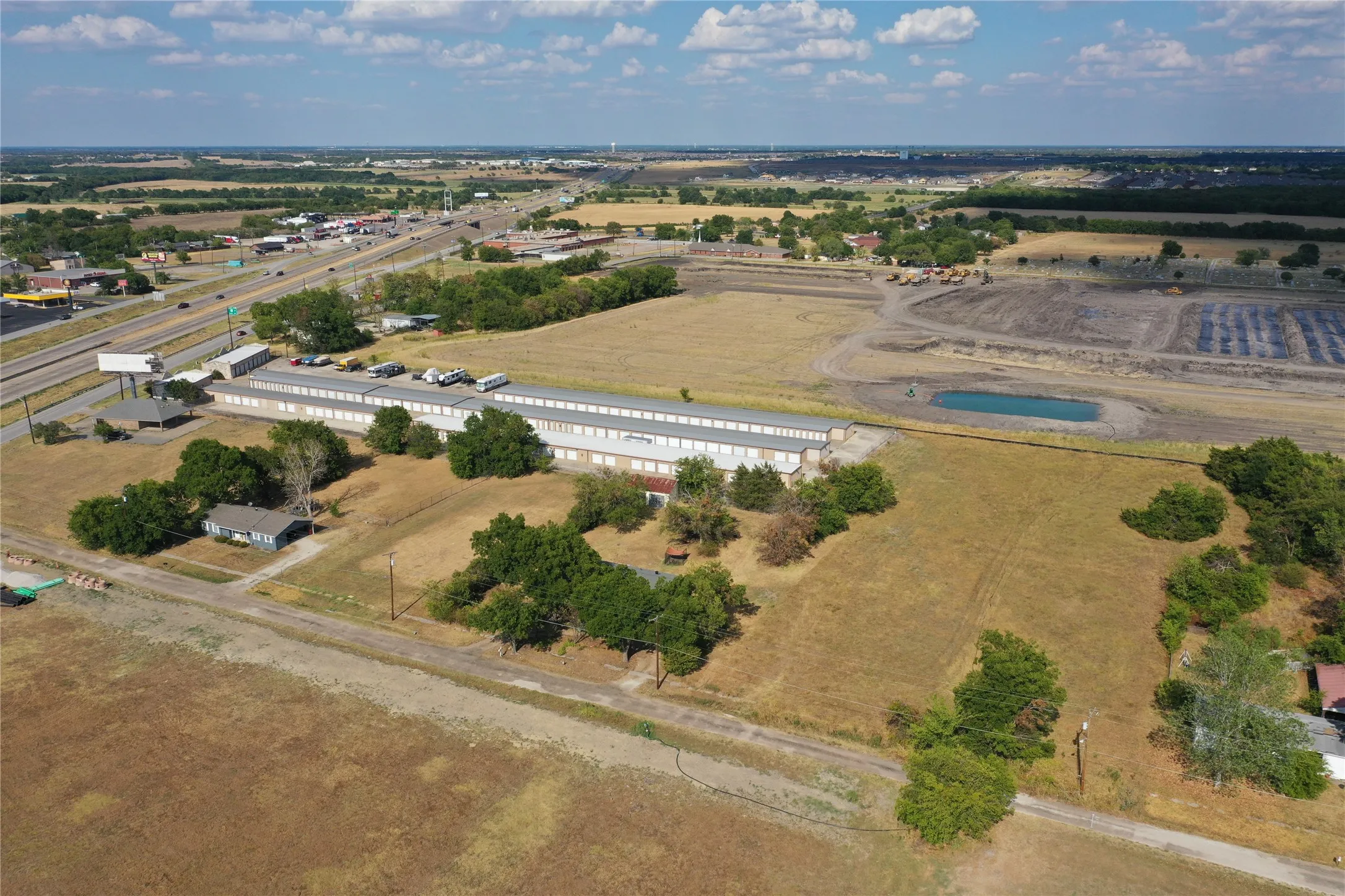 Expansive commercial property featuring a long-form building, paved parking areas, and surrounding undeveloped land