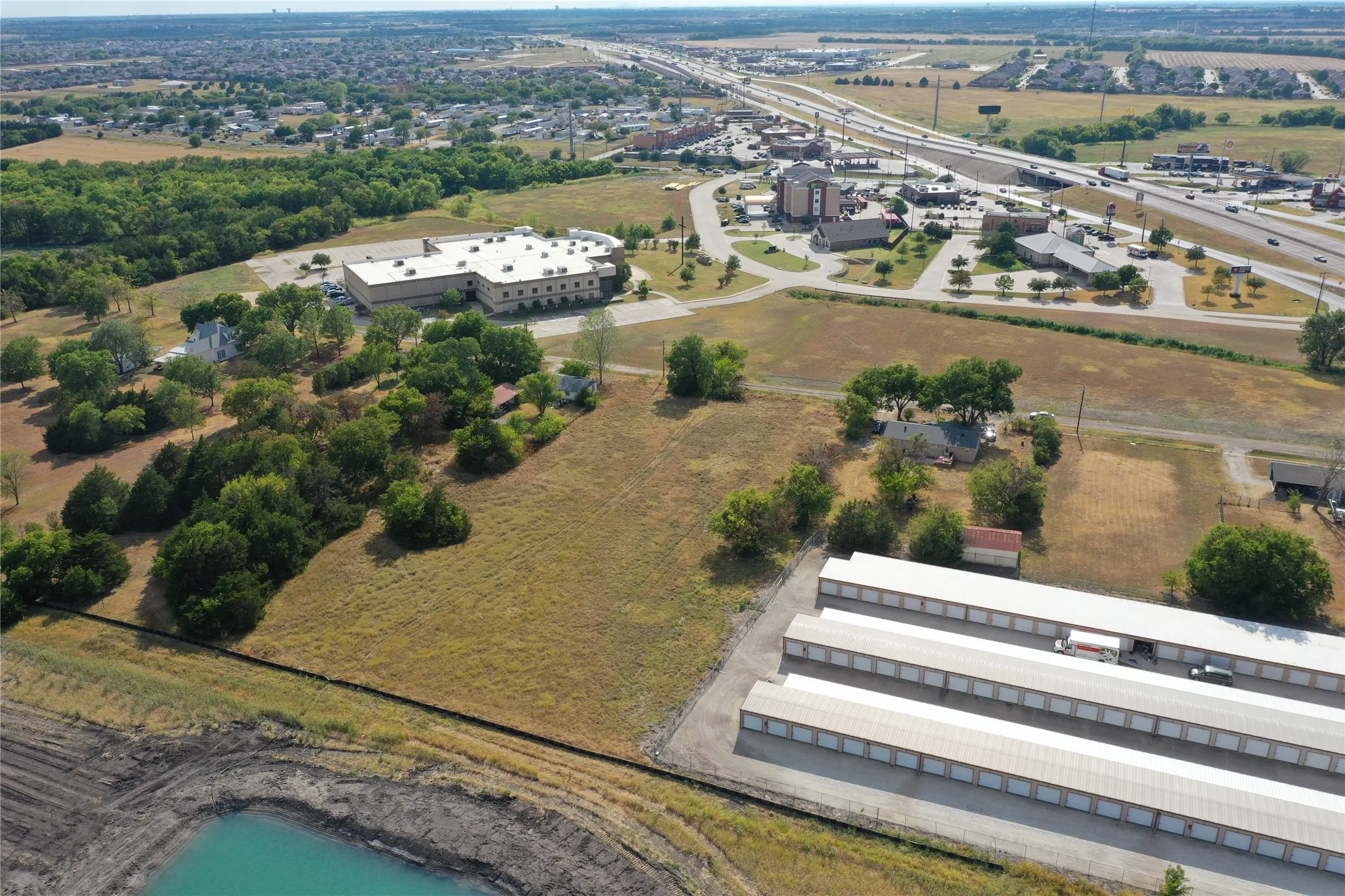 Expansive land parcel featuring open fields, a natural pond, mature trees, and proximity to highway infrastructure