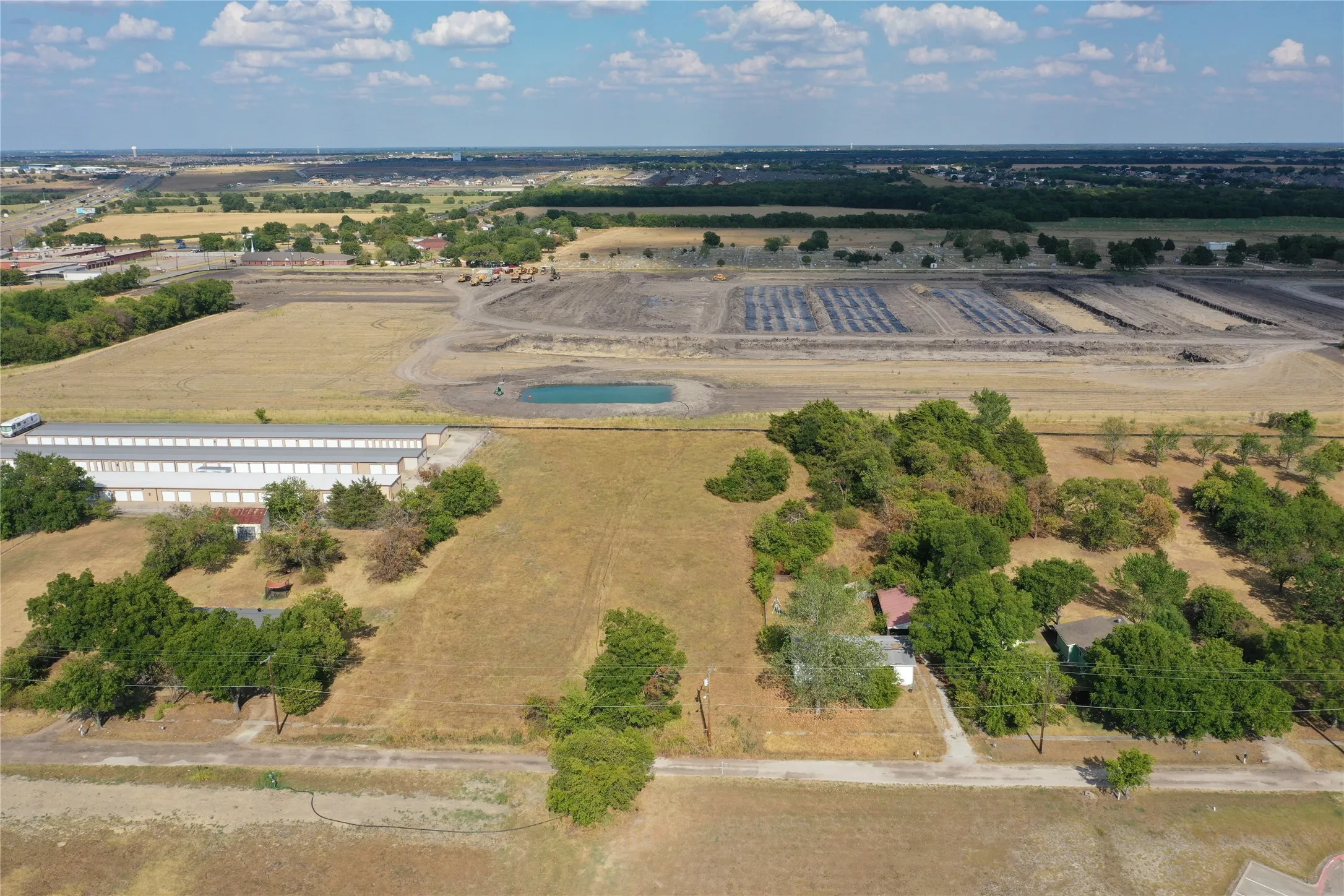 Expansive land parcel featuring open fields, scattered mature trees, a visible pond, and existing structures
