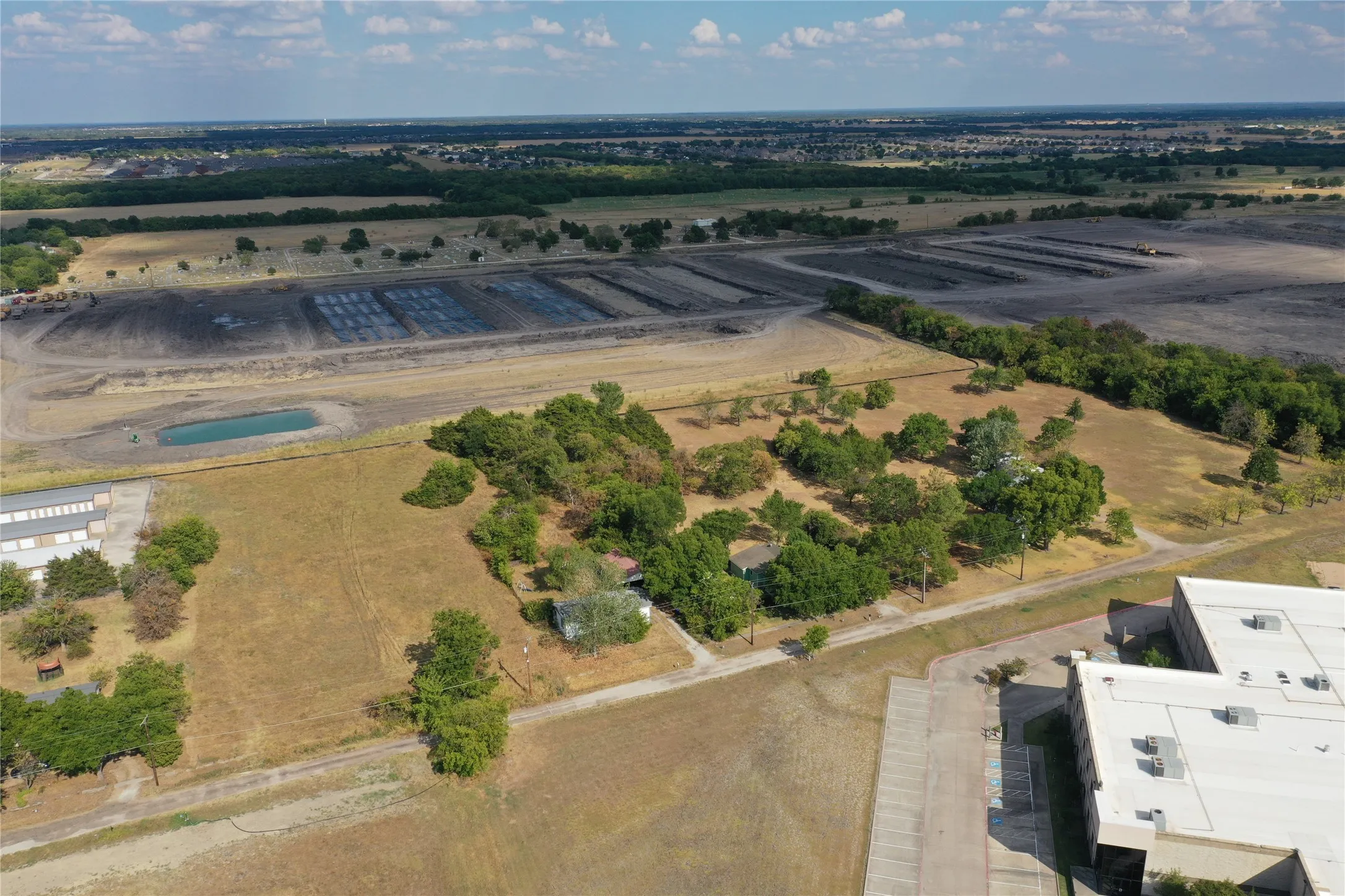 Expansive aerial property featuring large open land, a visible pond, perimeter trees, and a distant structure