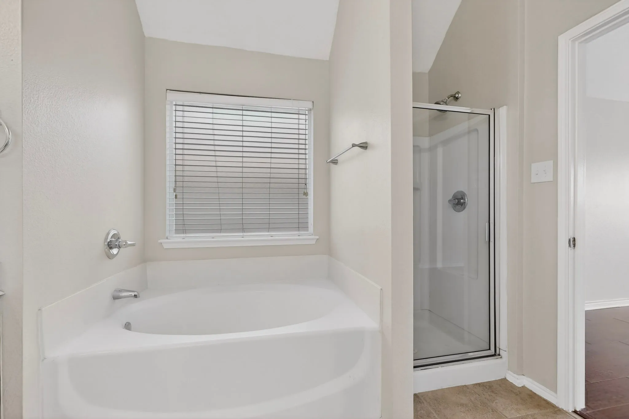 Bathroom featuring a corner soaking tub with chrome fixtures, a separate glass-enclosed shower, a window with horizontal blinds, and neutral wall tones