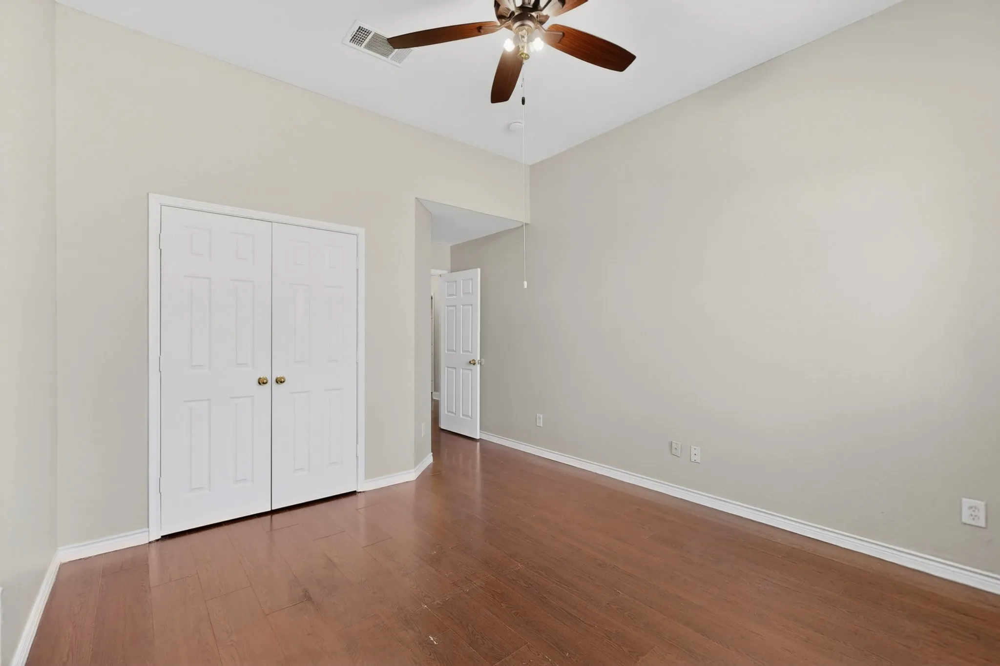 Room featuring high vaulted ceilings, wood-finish flooring, white trim, white paneled bifold doors, and a ceiling fan with light fixture