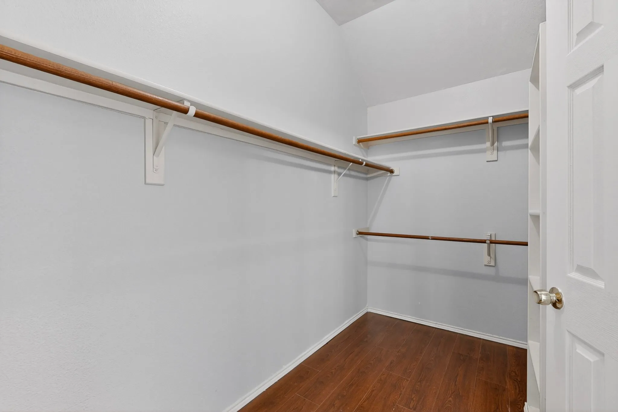Walk-in closet featuring wood-finish flooring, white walls, and multiple clothes rods with integrated shelving