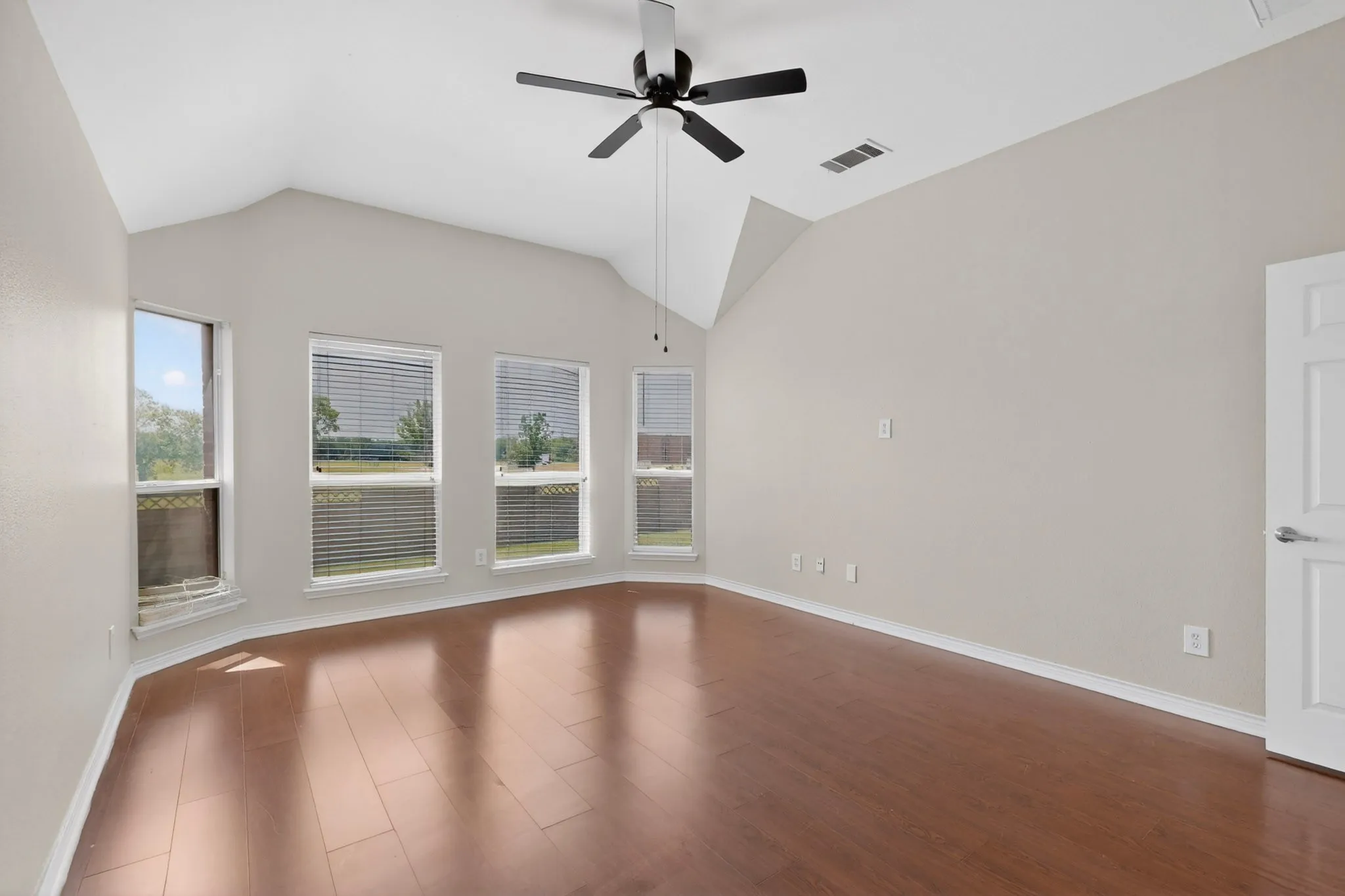 Vaulted ceiling room featuring a bay window with multiple vertical windows, wood-finish flooring, and a ceiling fan with integrated lighting