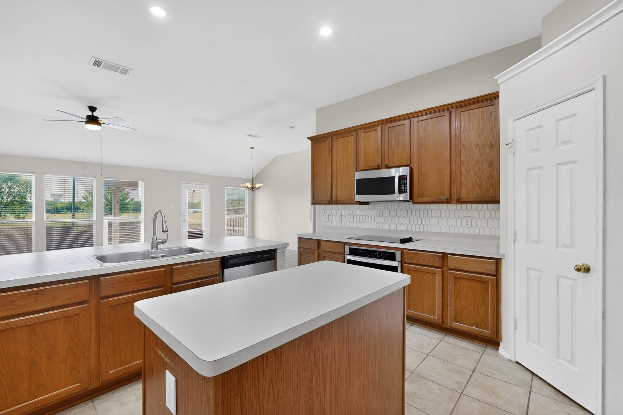 Kitchen featuring wood cabinetry, white countertops, a central island, stainless steel appliances, and a white picket tile backsplash