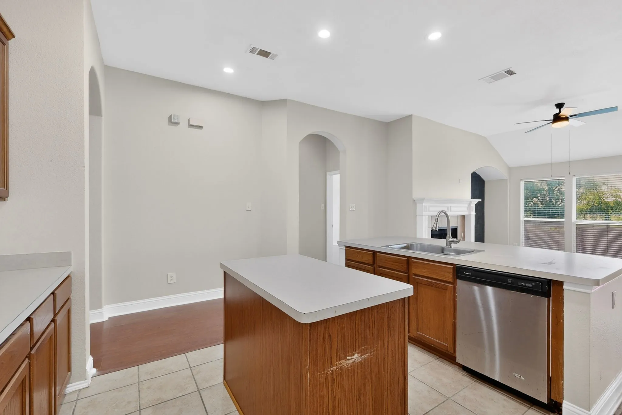 Open-concept kitchen featuring an island, light-toned countertops, wood-finish cabinetry, and stainless-steel appliances