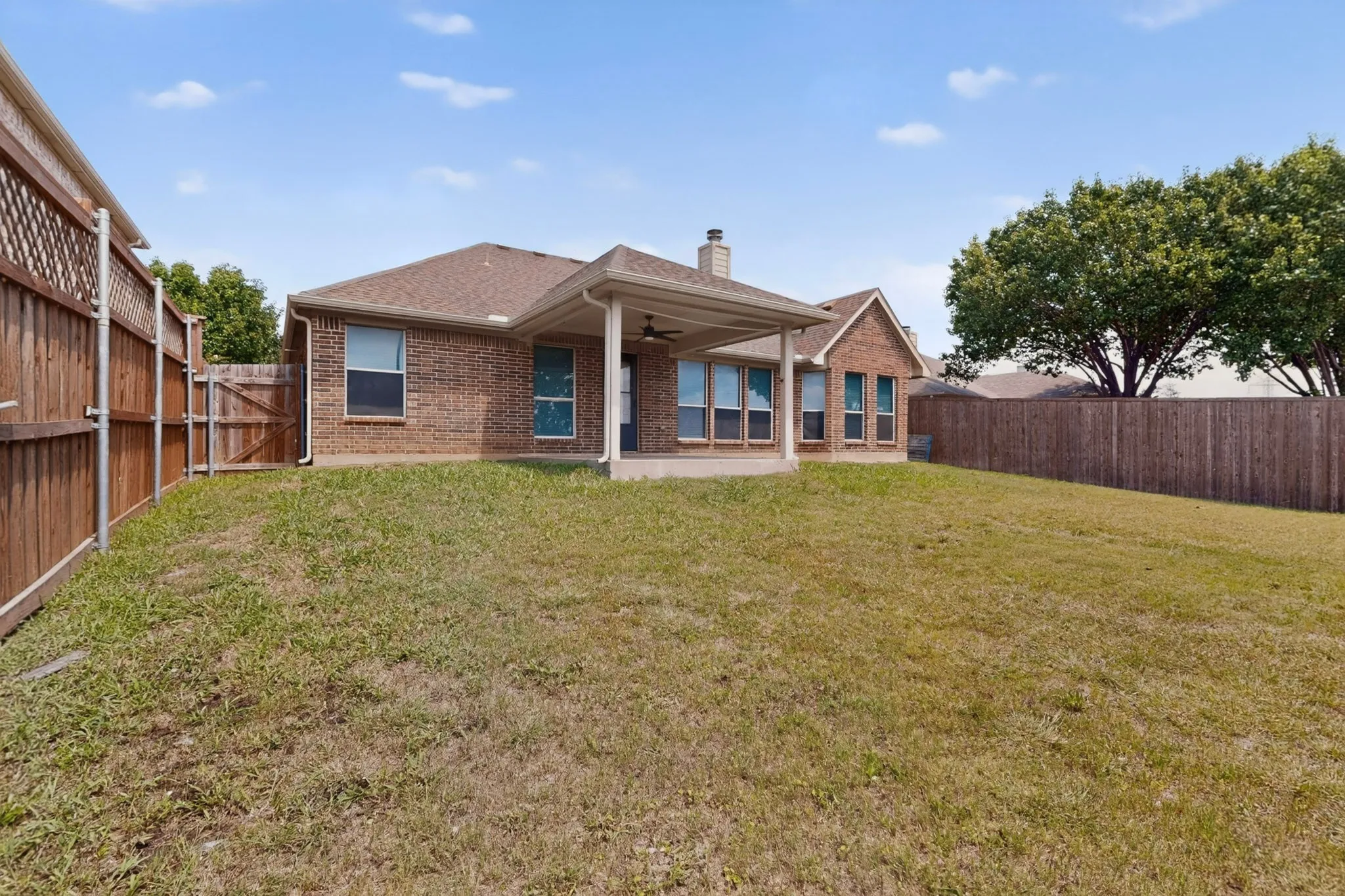 Expansive backyard featuring a covered patio, brick exterior, multiple windows, and privacy fencing