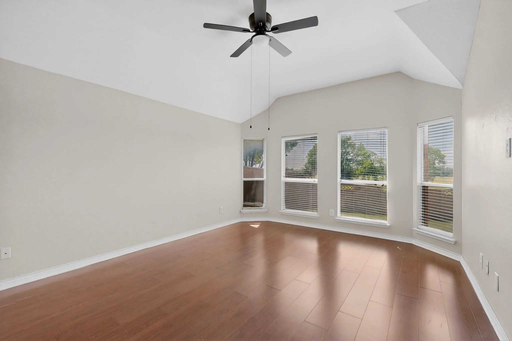 Expansive room featuring vaulted ceilings, wood-finish flooring, a contemporary ceiling fan, and multiple windows providing ambient light