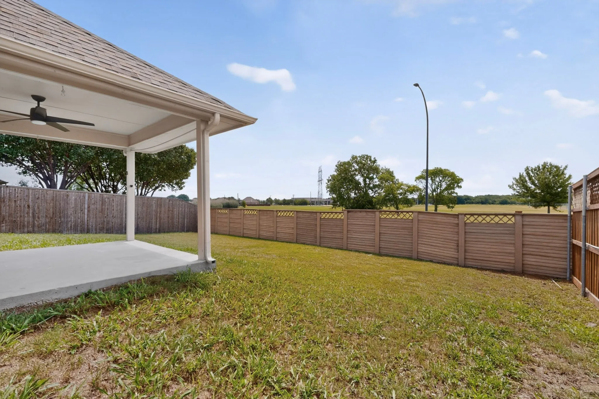 Expansive backyard featuring a covered patio with a ceiling fan, a concrete patio slab, a multi-panel wood fence, and a decorative slatted wood fence