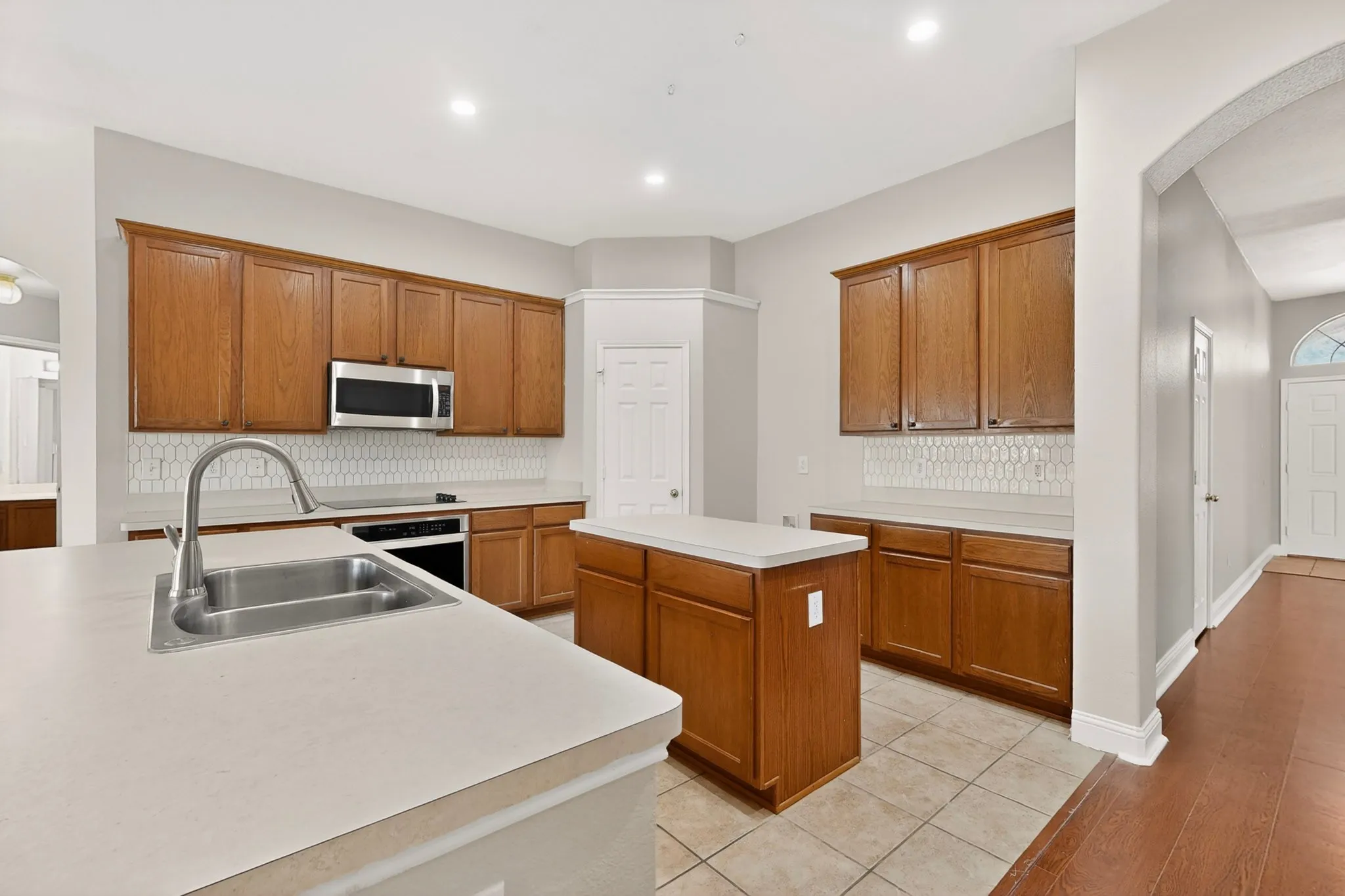 Kitchen featuring honey-toned wood cabinetry, stainless steel appliances, and a white geometric tile backsplash