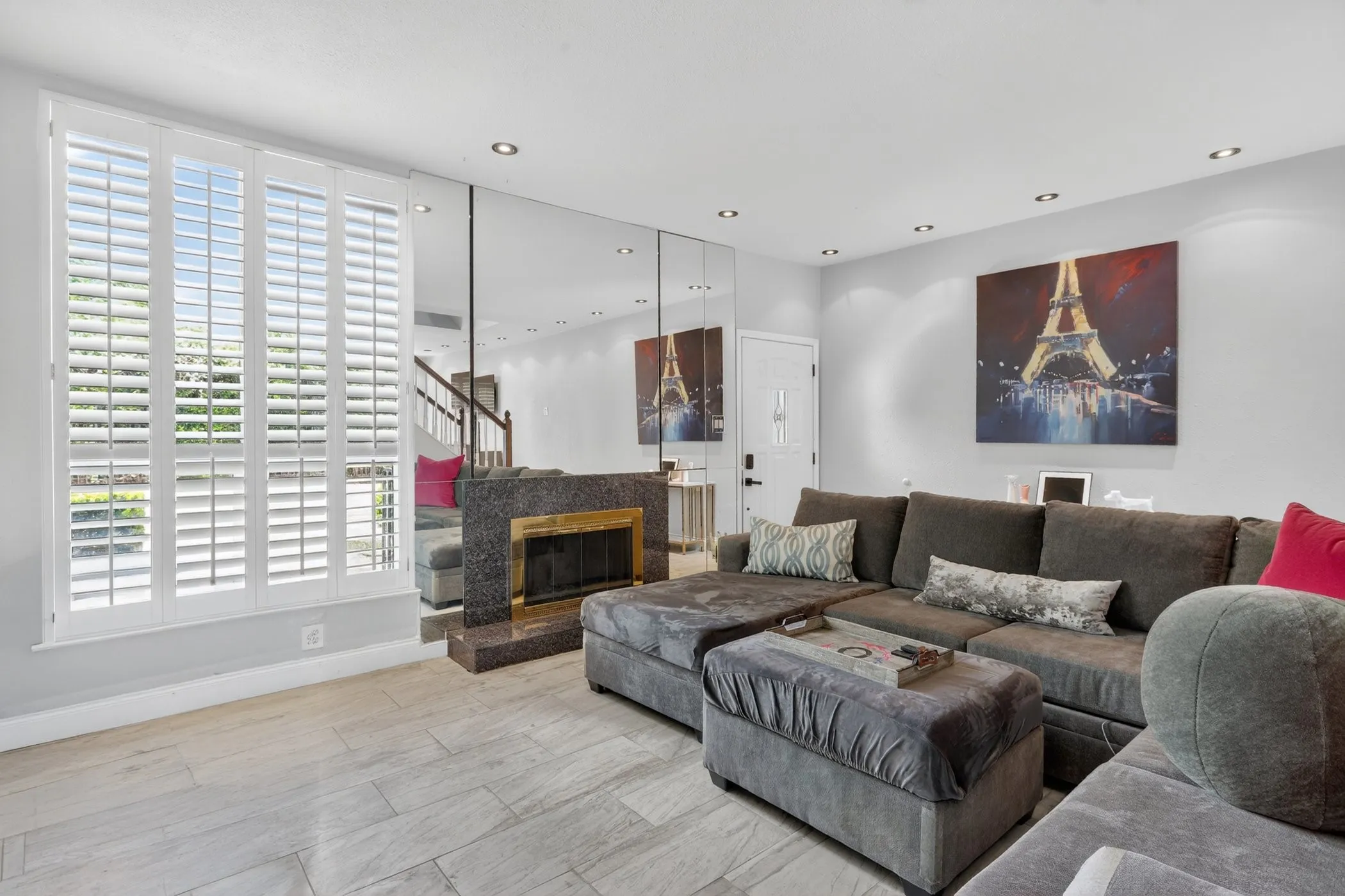 Living area featuring wide plank tile flooring, a fireplace with a stone surround, a mirrored accent wall, recessed lighting, and plantation shutters