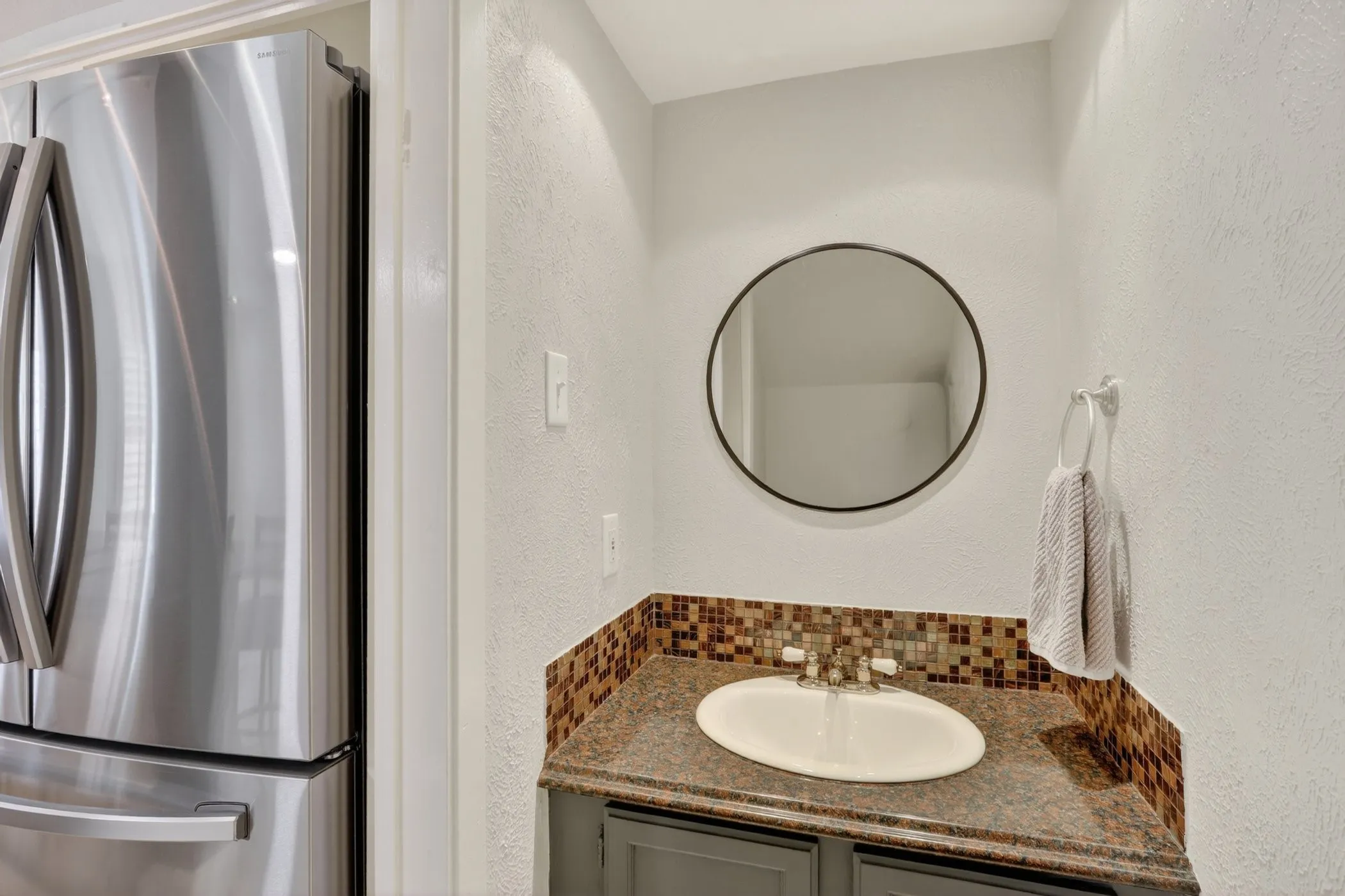 Vanity featuring an oval undermount sink, granite-style countertop, and mosaic tile backsplash