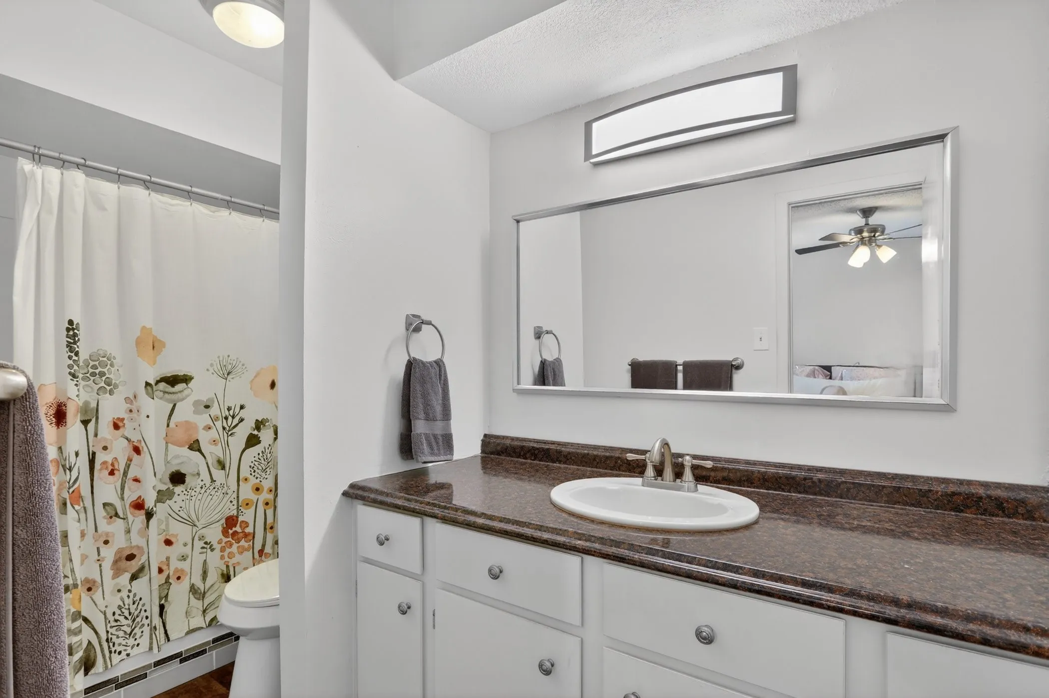 Bathroom featuring a white vanity with silver hardware, a single basin sink, a dark countertop, and a large wall mirror