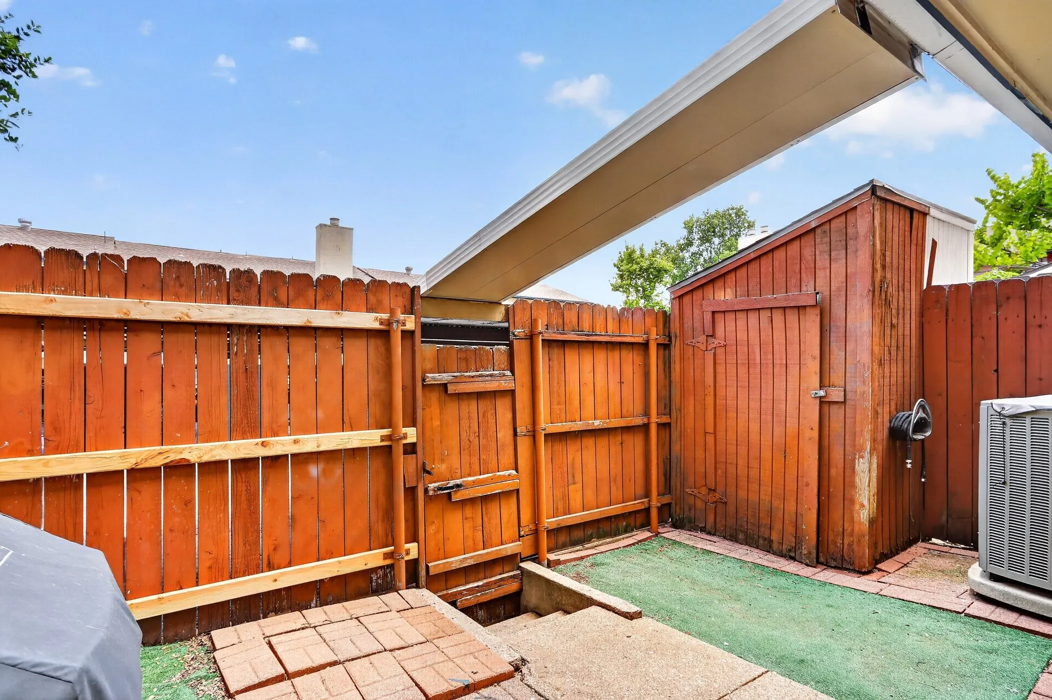Fenced outdoor area featuring a storage shed, brick paver accents, and a concrete patio section