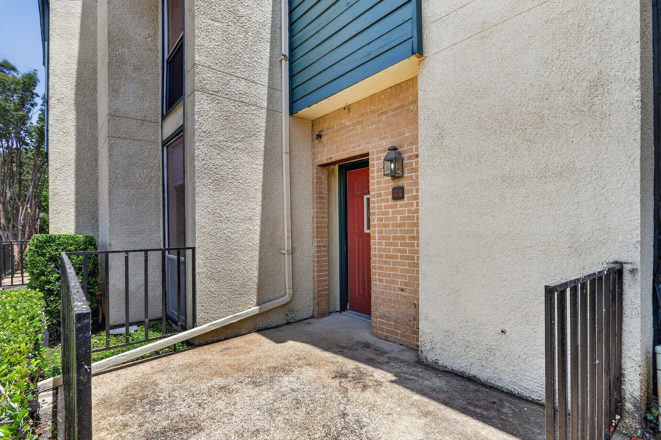 Exterior entrance featuring a red door, brick facade, wall-mounted lantern, and textured stucco siding