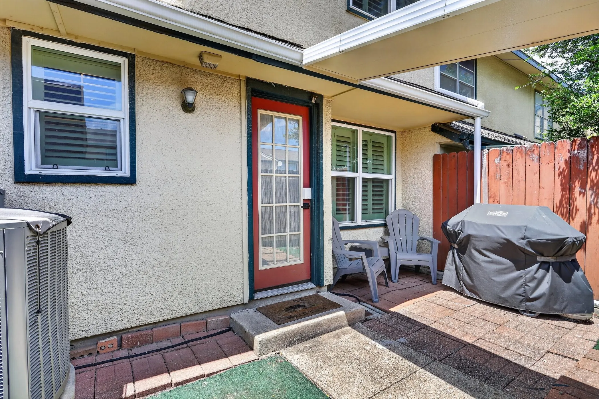 Private patio space featuring a red paneled door, shuttered windows, and a partially covered area