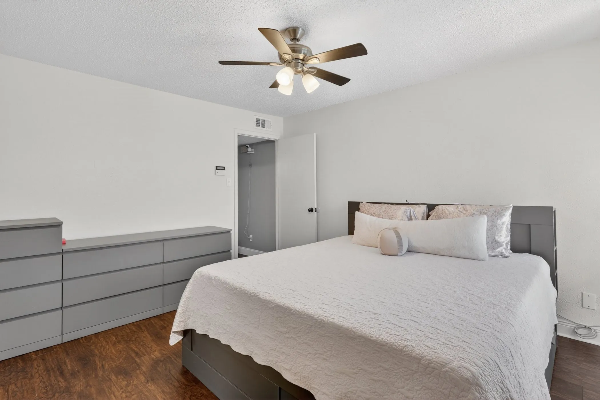 Room featuring wood-finish flooring, a ceiling fan with integrated lighting, and a white door with dark hardware