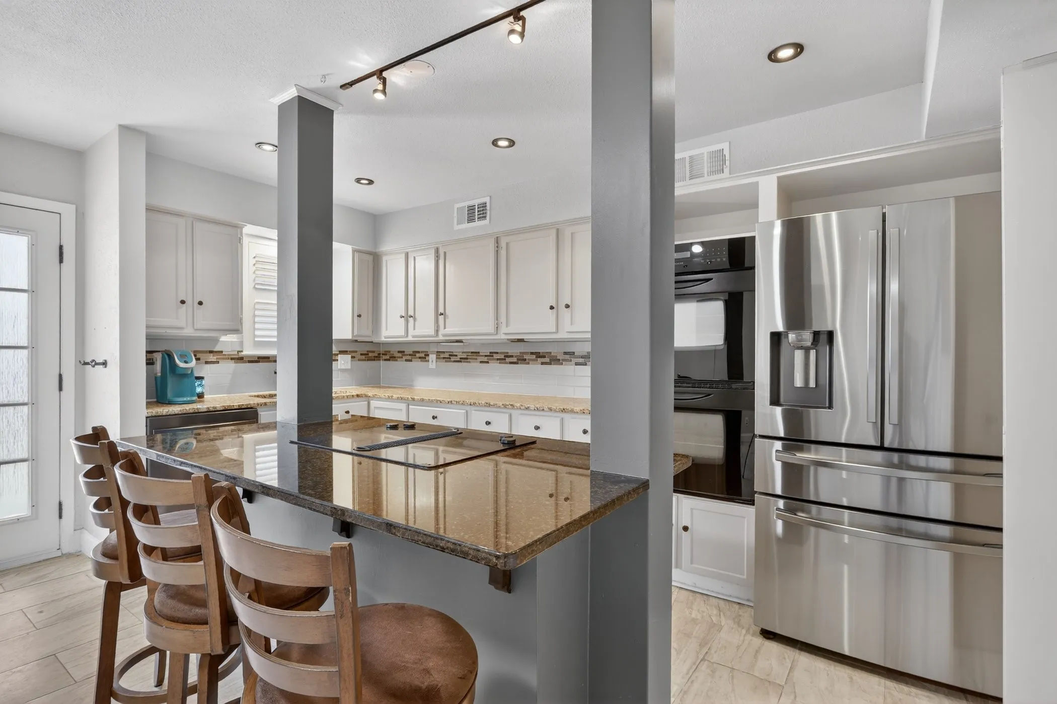Kitchen featuring a granite-topped island with cooktop, white cabinetry, stainless steel French door refrigerator, and double wall ovens