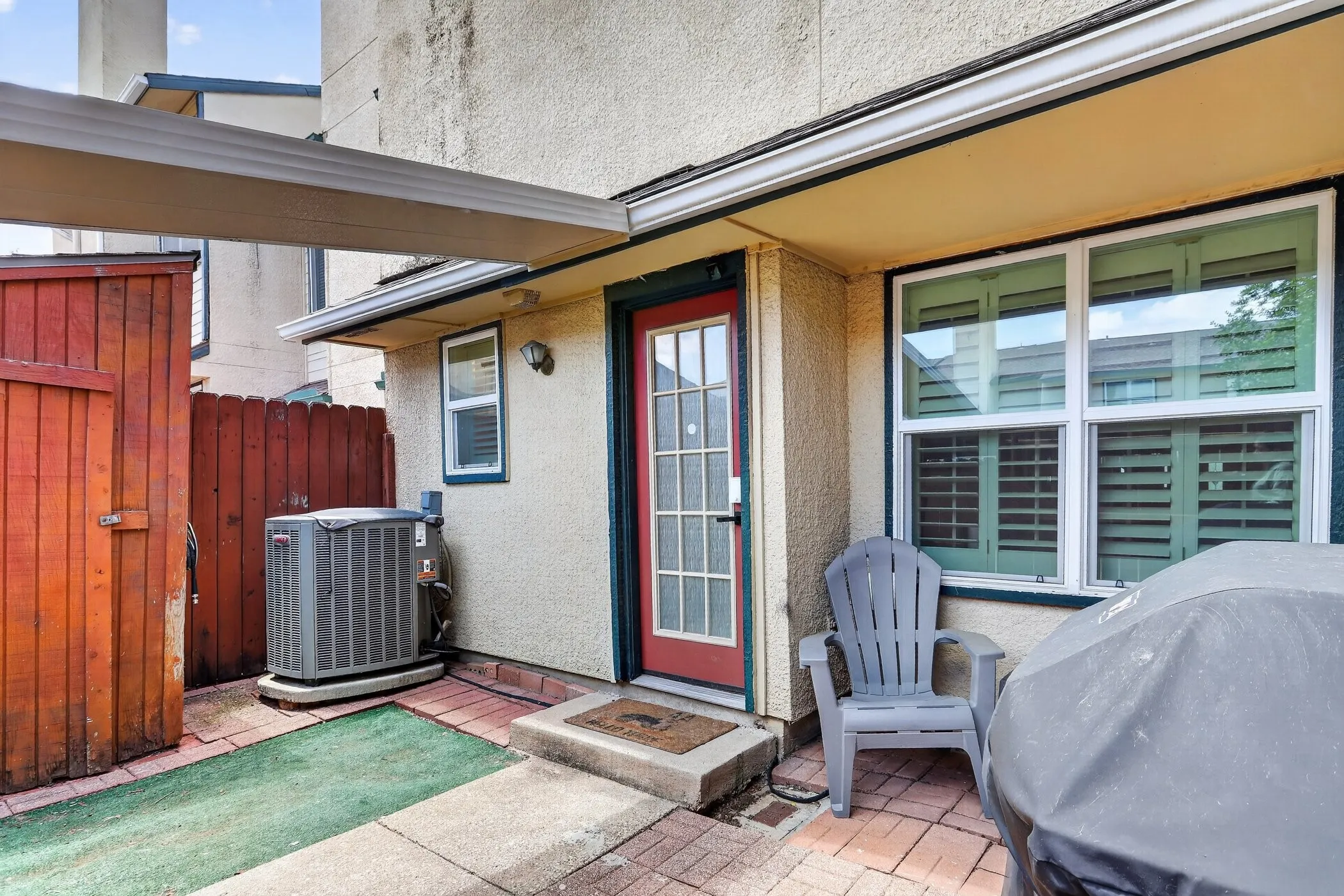 Private patio space featuring brick paver flooring, an awning, and a red entry door with glass panels
