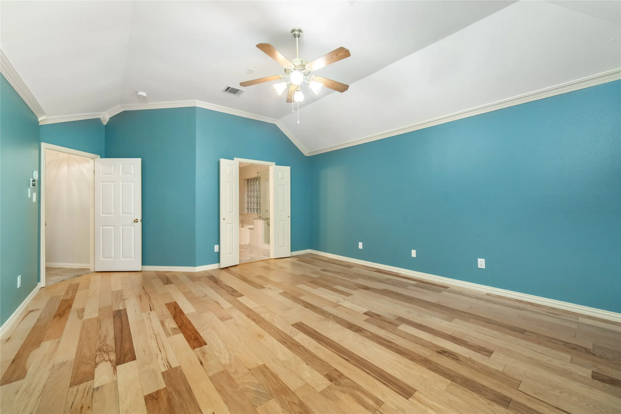 Spacious room featuring wood-finish flooring, vaulted ceilings, a ceiling fan with light fixture, and two sets of double doors
