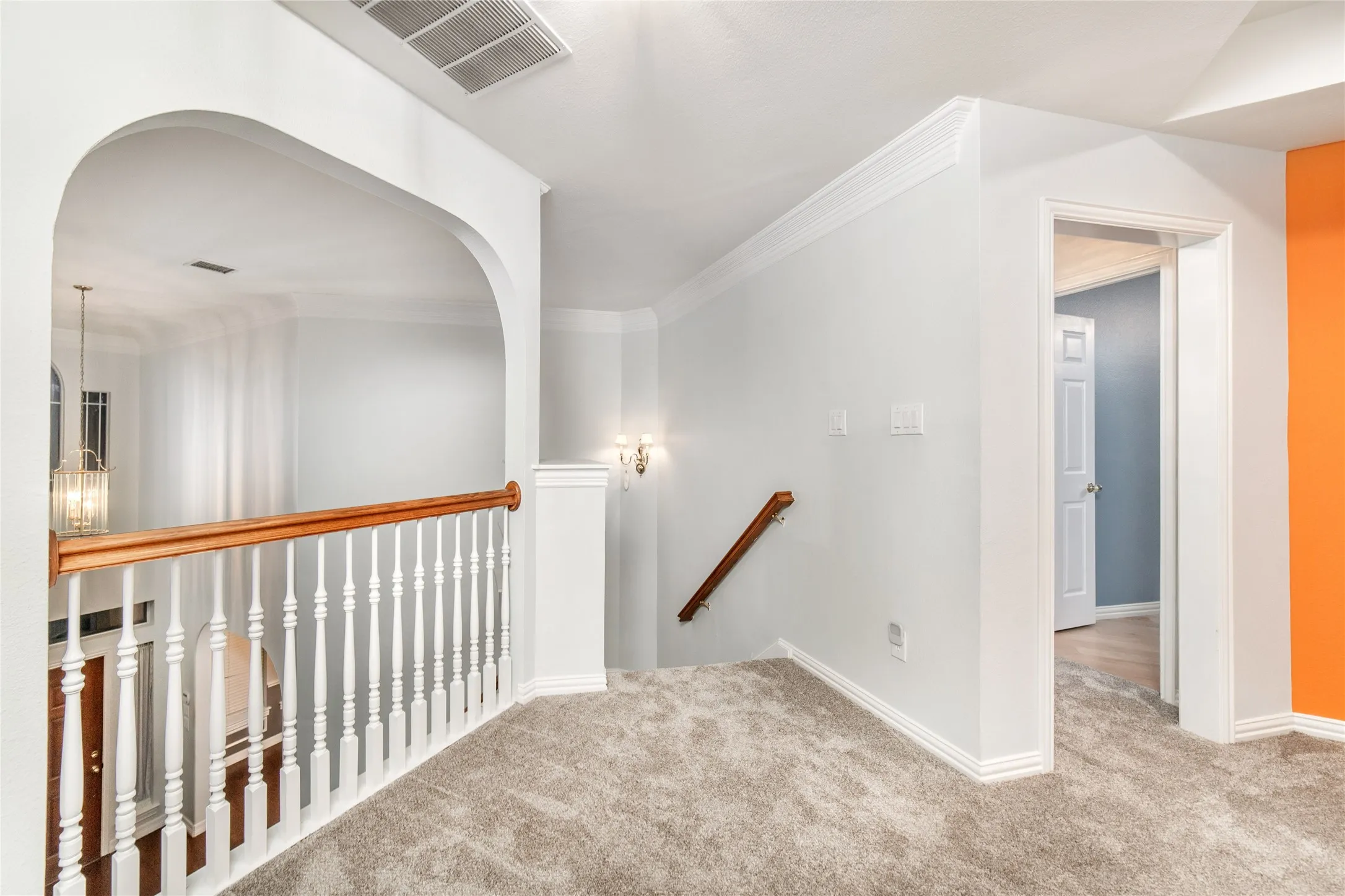 Carpeted upper-level landing featuring an arched opening, white balusters with a wood handrail, crown molding, and a built-in wall sconce