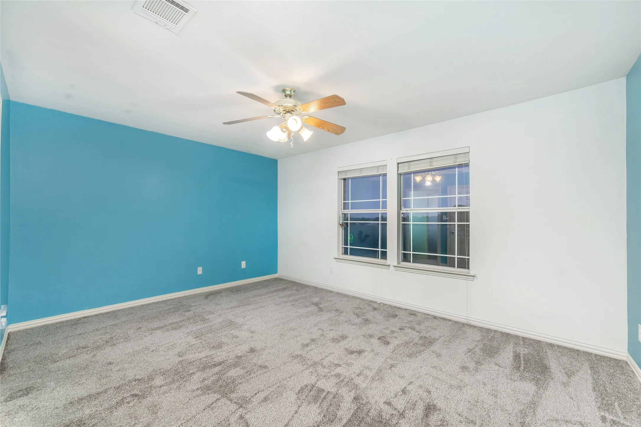 Spacious room featuring a blue accent wall, white walls, and gray carpet flooring