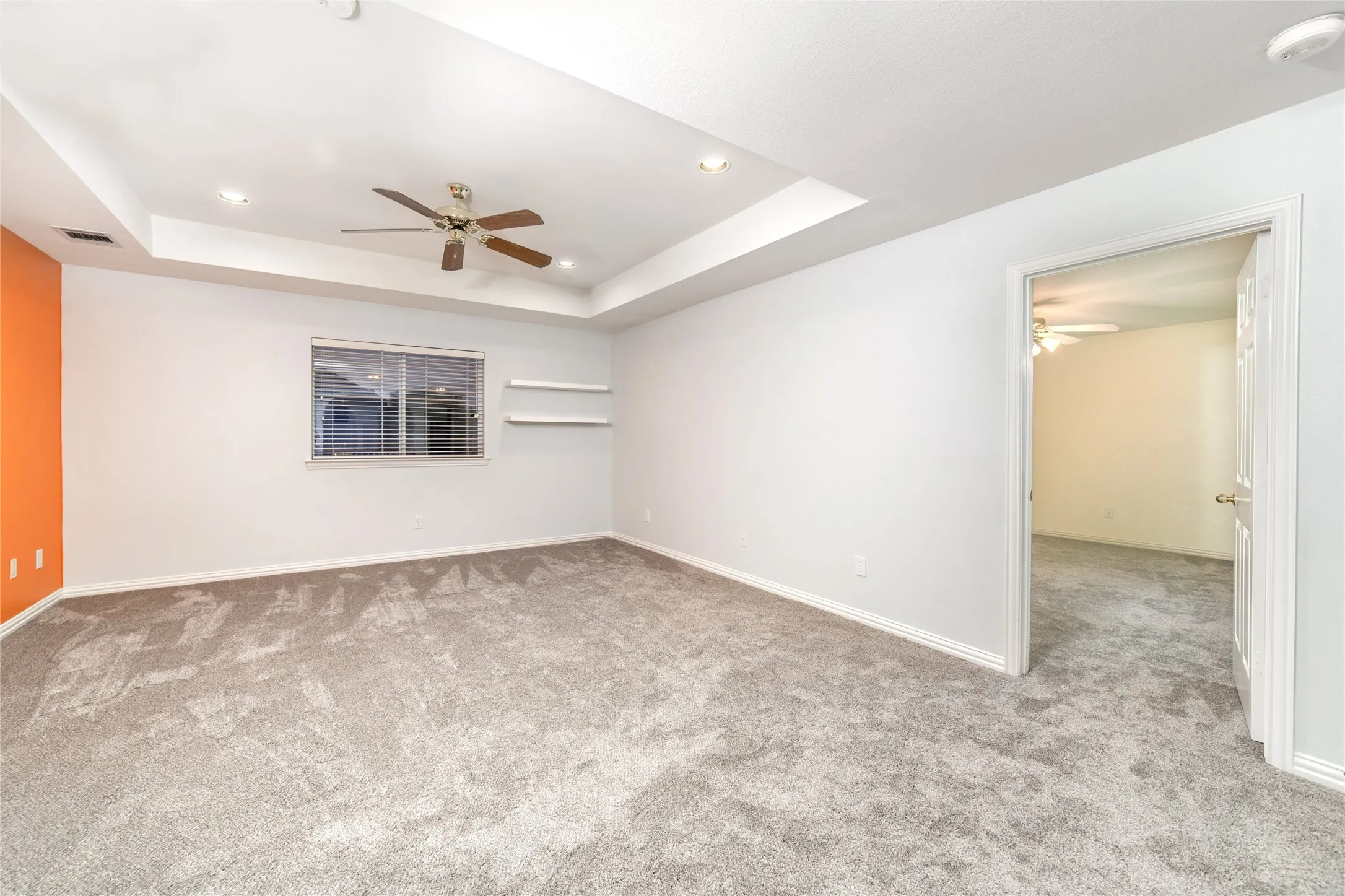 Spacious room featuring tray ceilings with recessed lighting, a ceiling fan, and carpet flooring