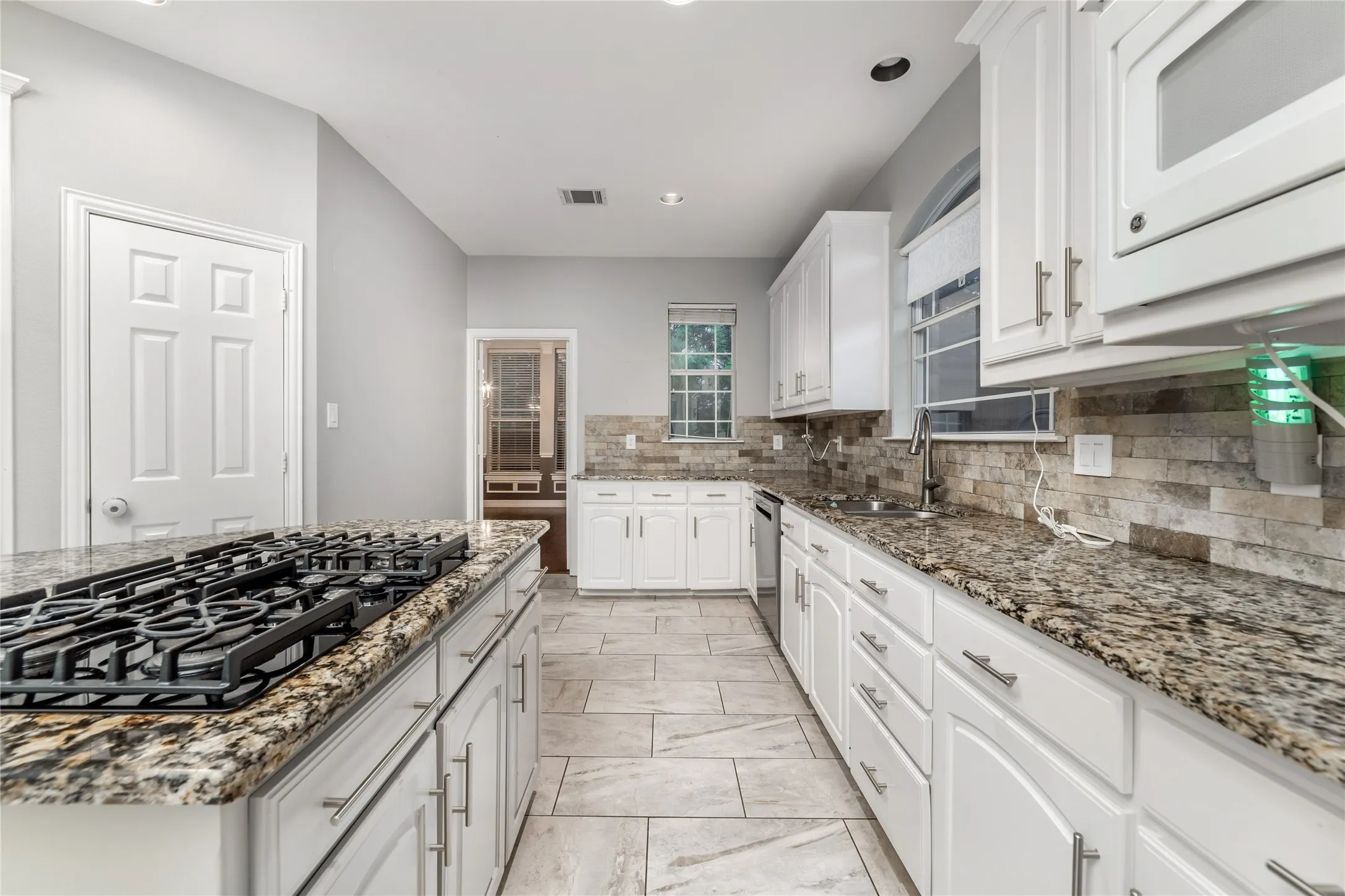 Galley kitchen featuring a gas range, stone countertops, white cabinetry with brushed nickel hardware, a stone tile backsplash, and light-toned tile flooring