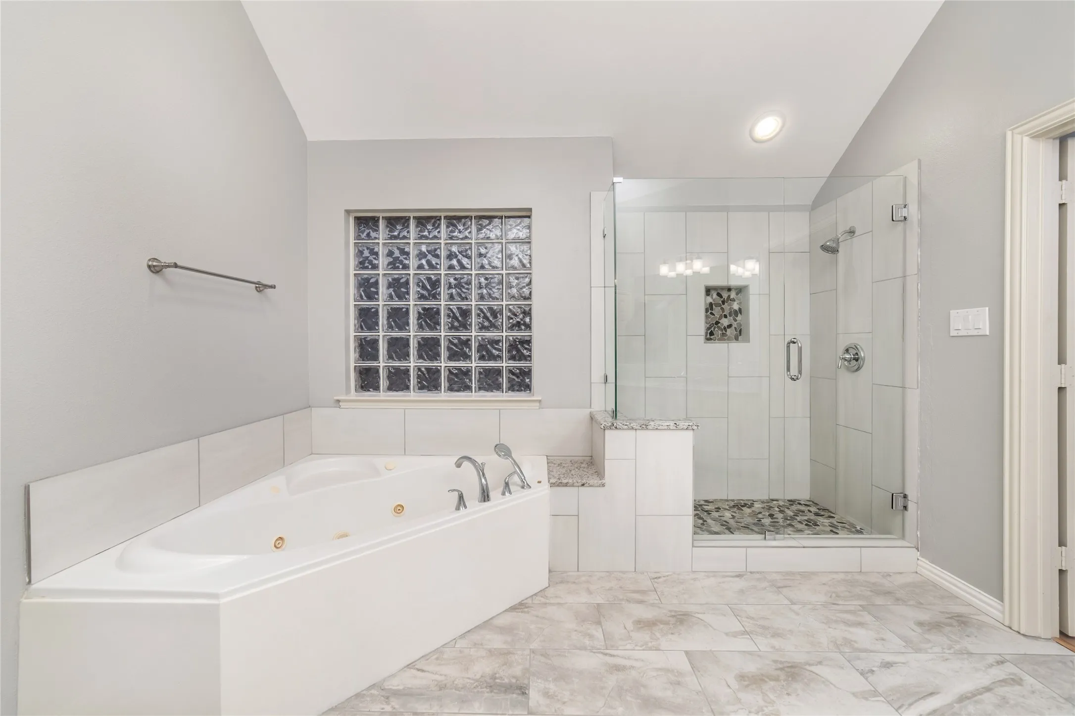 Corner jetted tub with a glass block window and a tiled surround