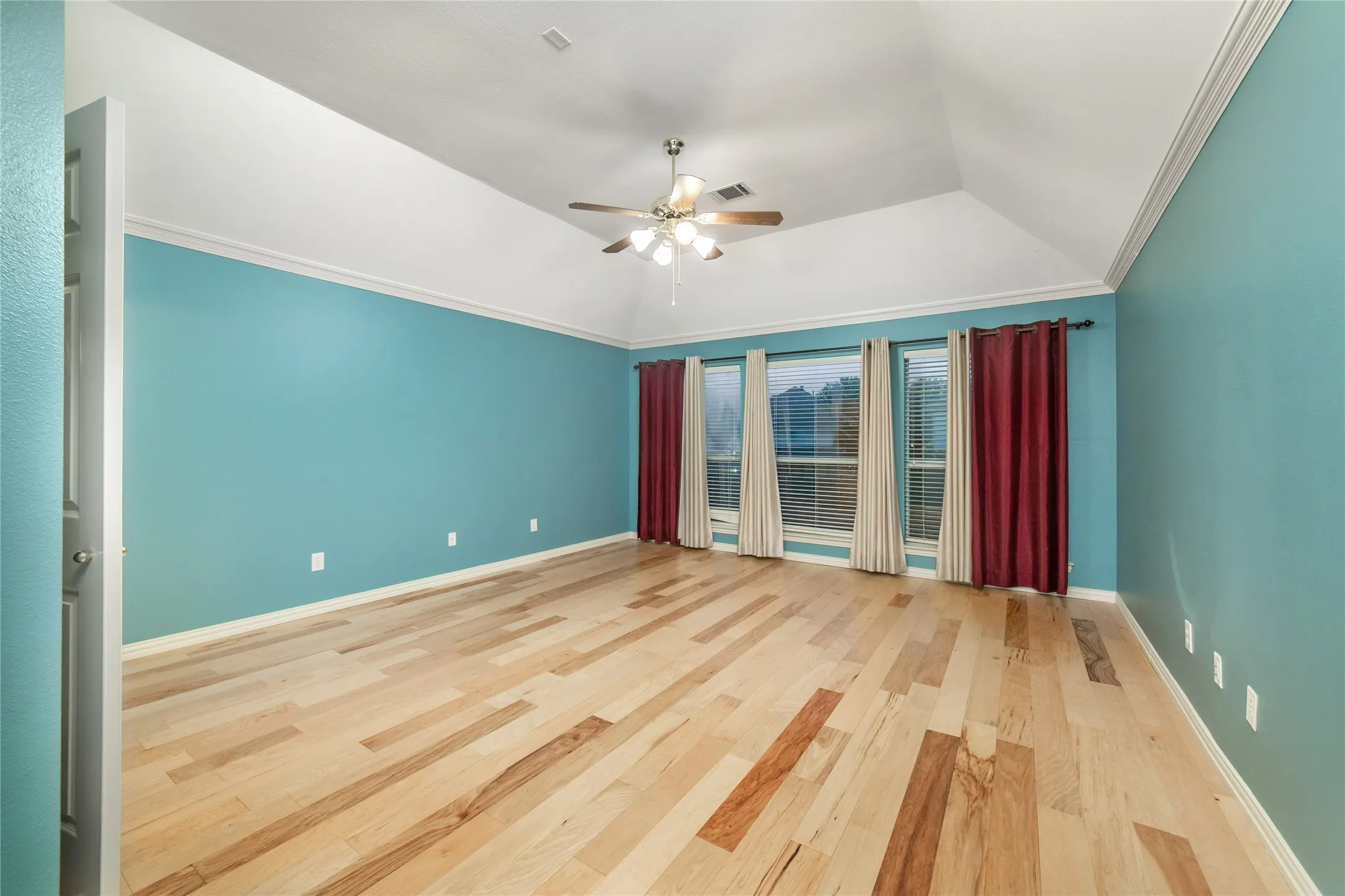 Spacious room featuring vaulted ceilings, light wood-finish flooring, and crown molding